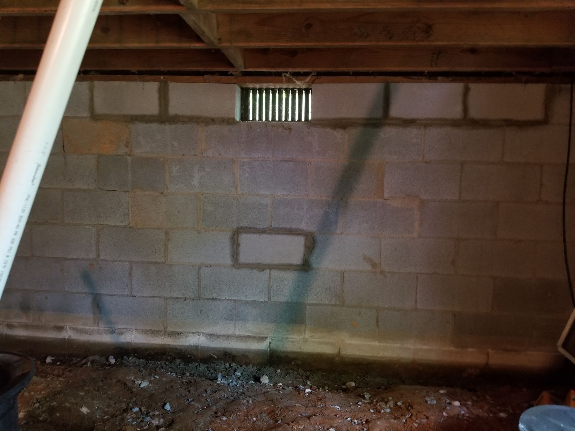 Basement wall with cinder blocks, wooden joists, and a small vent near the ceiling.