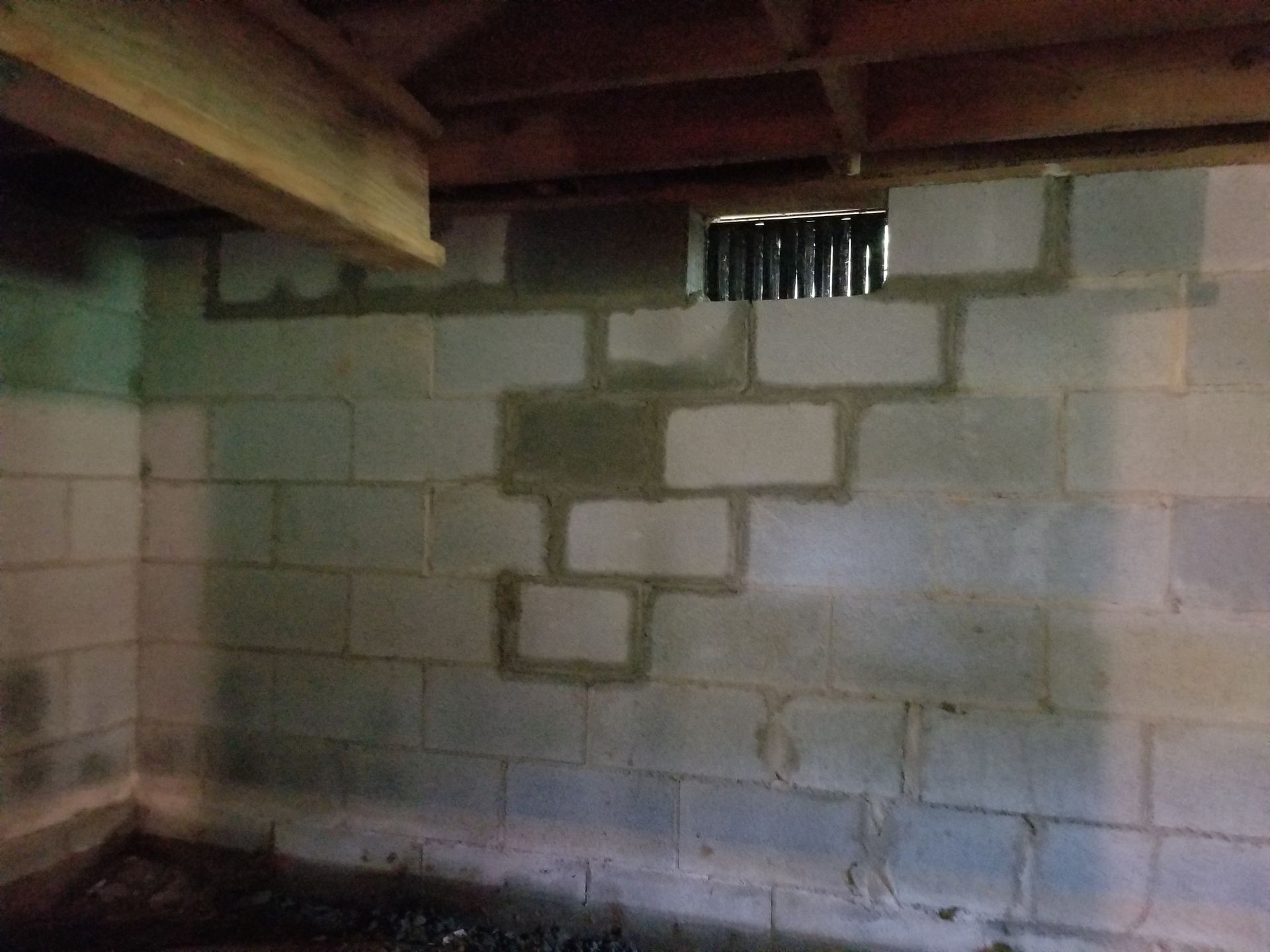 Dim basement wall with cinder blocks, exposed ceiling beams, and a small vent near the top.
