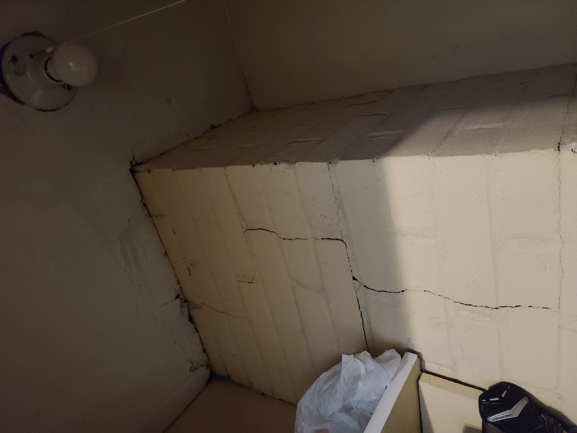 Tiled bathroom wall with visible cracks; cleaning supplies sit on the floor below.