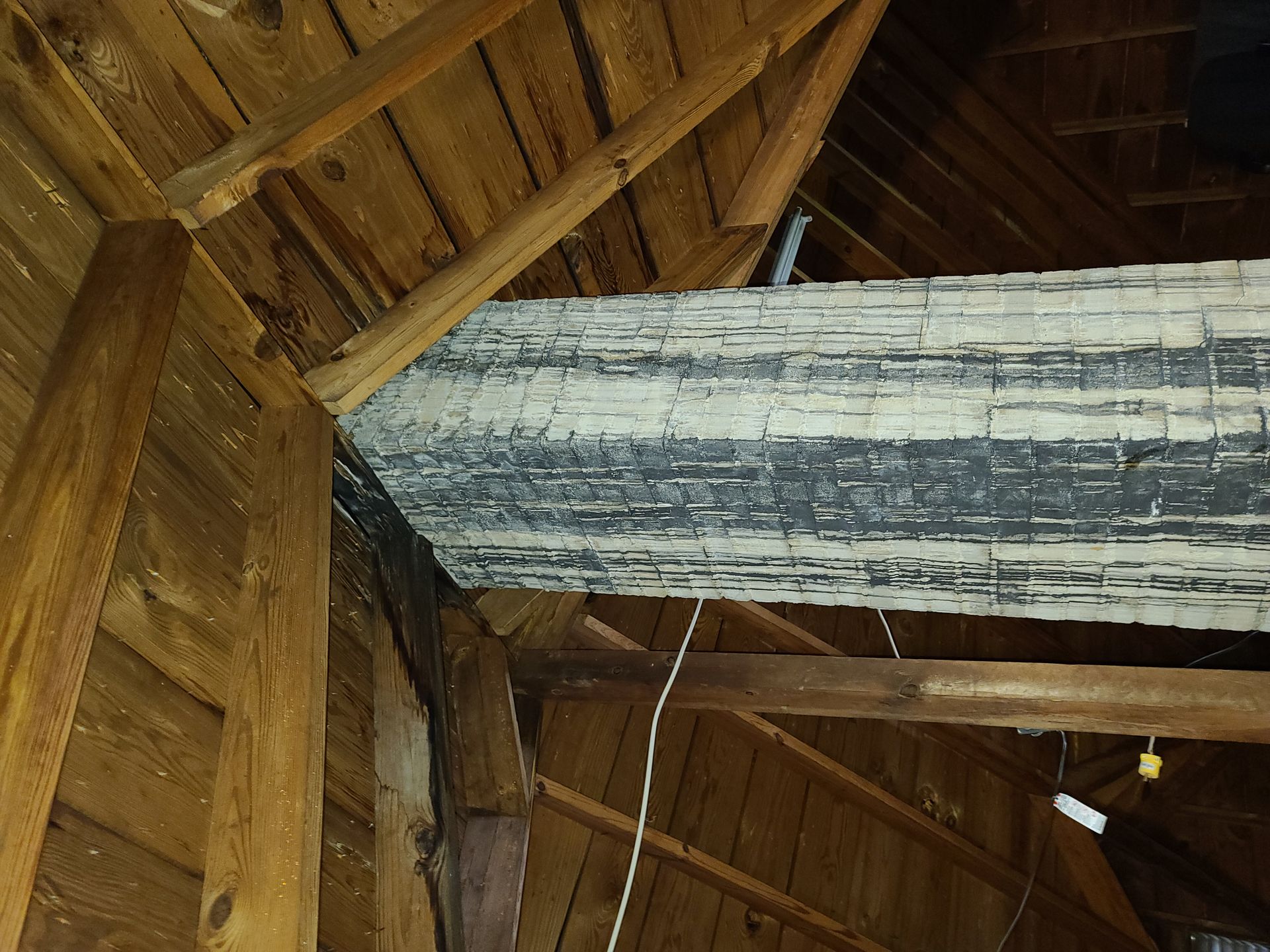 Wooden roof beams with a weathered white-and-gray log under a thatched ceiling