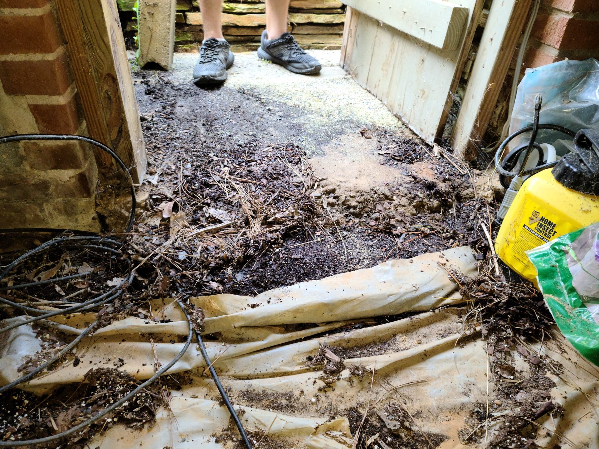Muddy doorway with damaged floor and debris, with shoes visible in the background