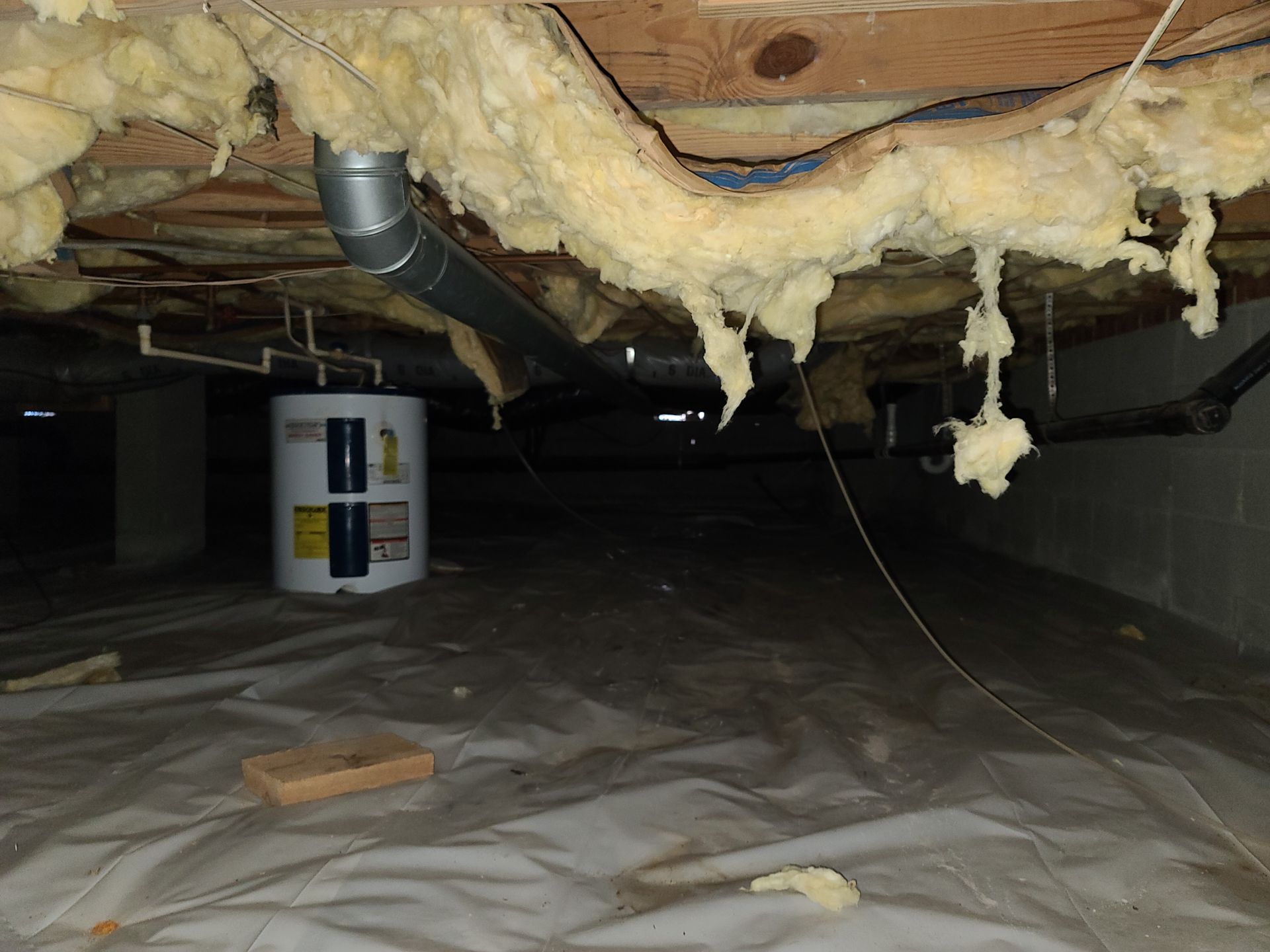 Crawlspace with exposed insulation, plastic ground cover, and a water heater in the background