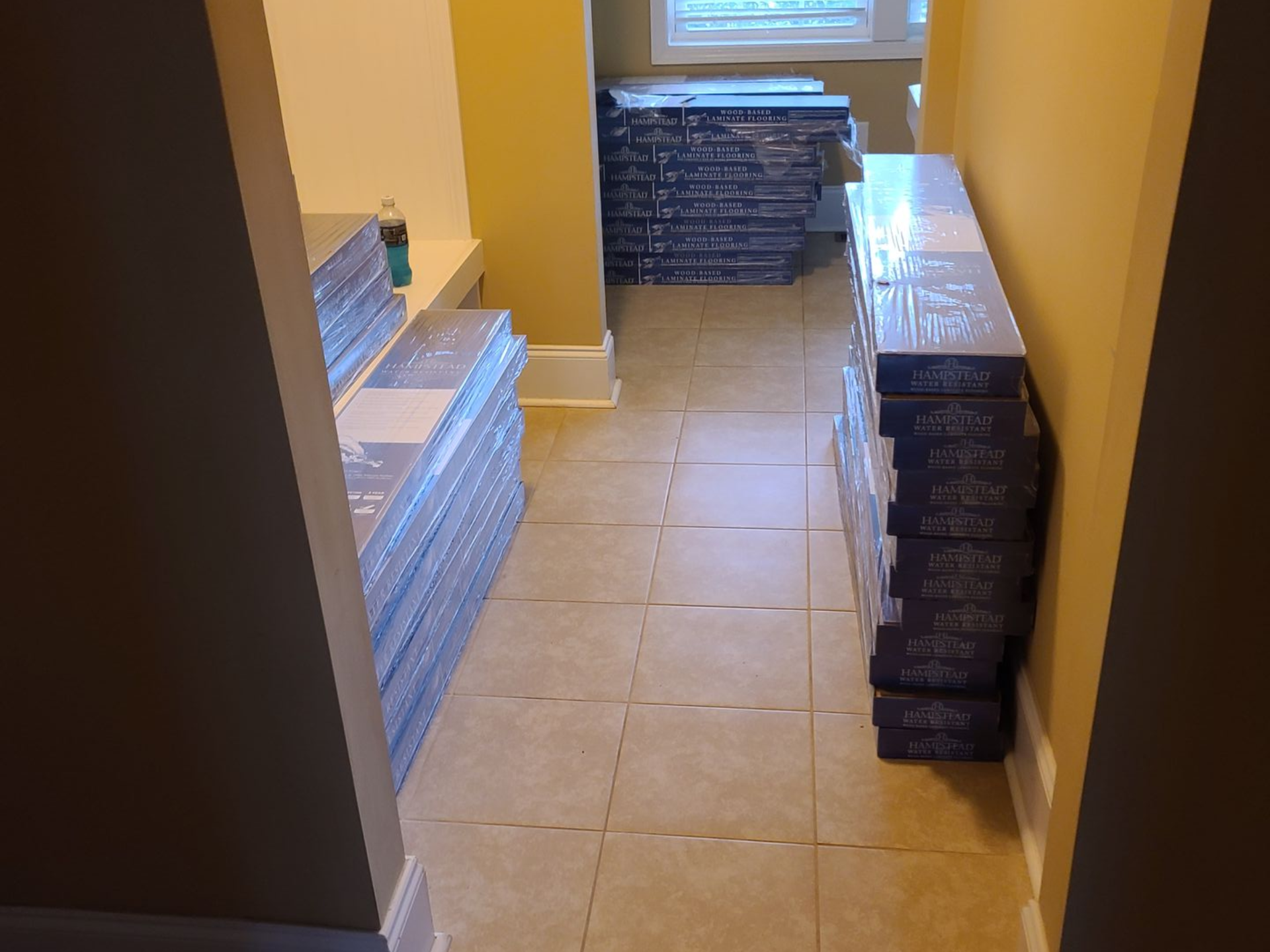Hallway with stacked construction materials and boxes on both sides of a tiled floor