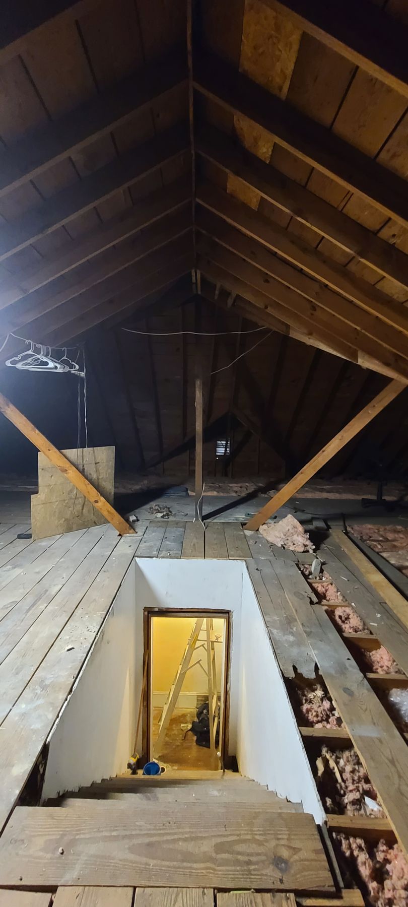 Attic interior with exposed rafters and insulation, showing a small rectangular access opening below.