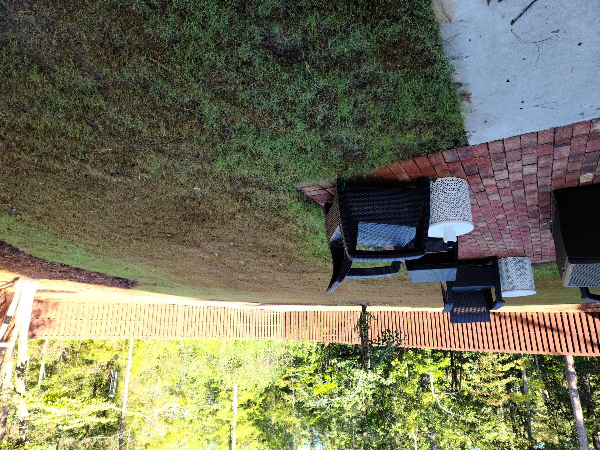 Backyard patio with black grill, brick walkway, hedge, and wooden fence in sunlight