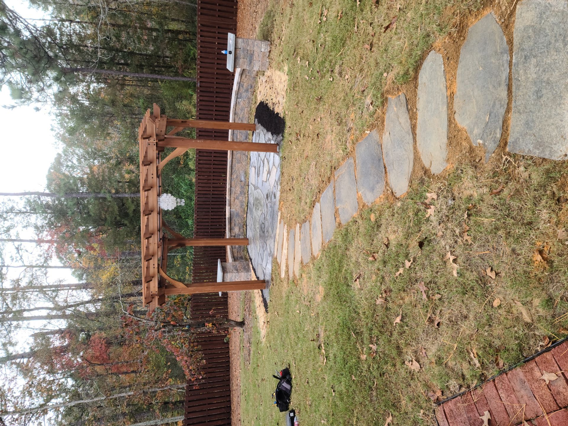 Backyard garden path with stepping stones, wooden pergola, and black chickens near a fence