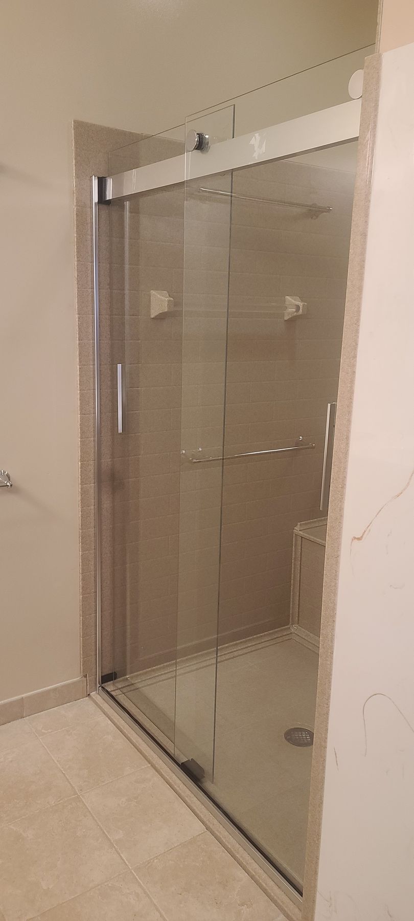 Glass shower enclosure with sliding door in a beige-tiled bathroom