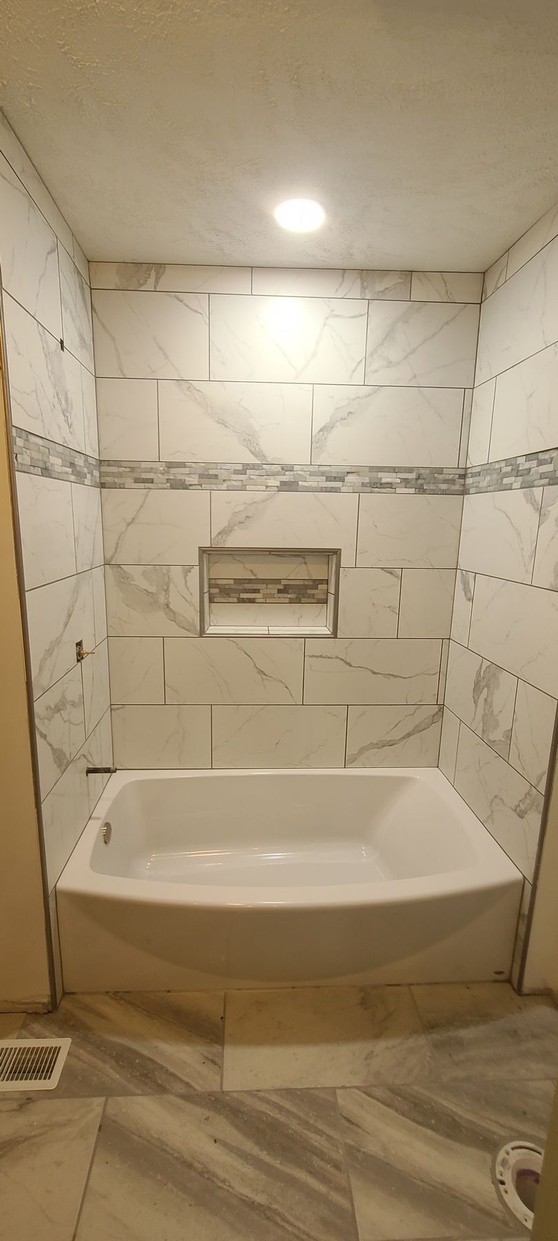 Modern tiled shower/tub alcove with a built-in niche and recessed ceiling light