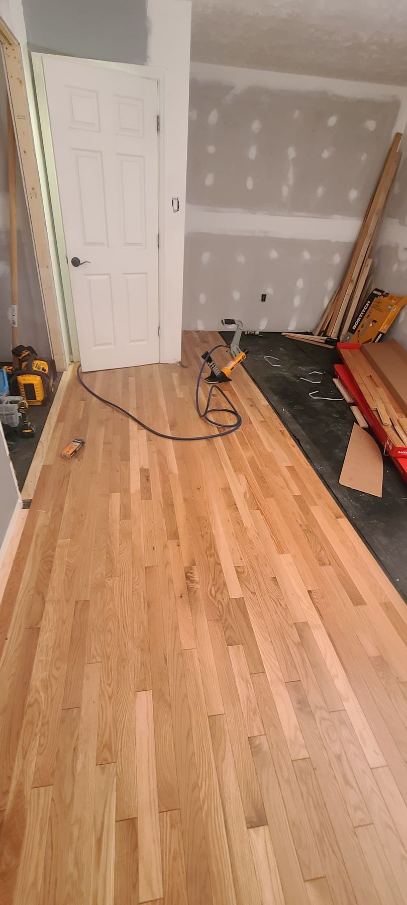 Renovation room with hardwood floor, drywall, and construction tools near a closed white door.