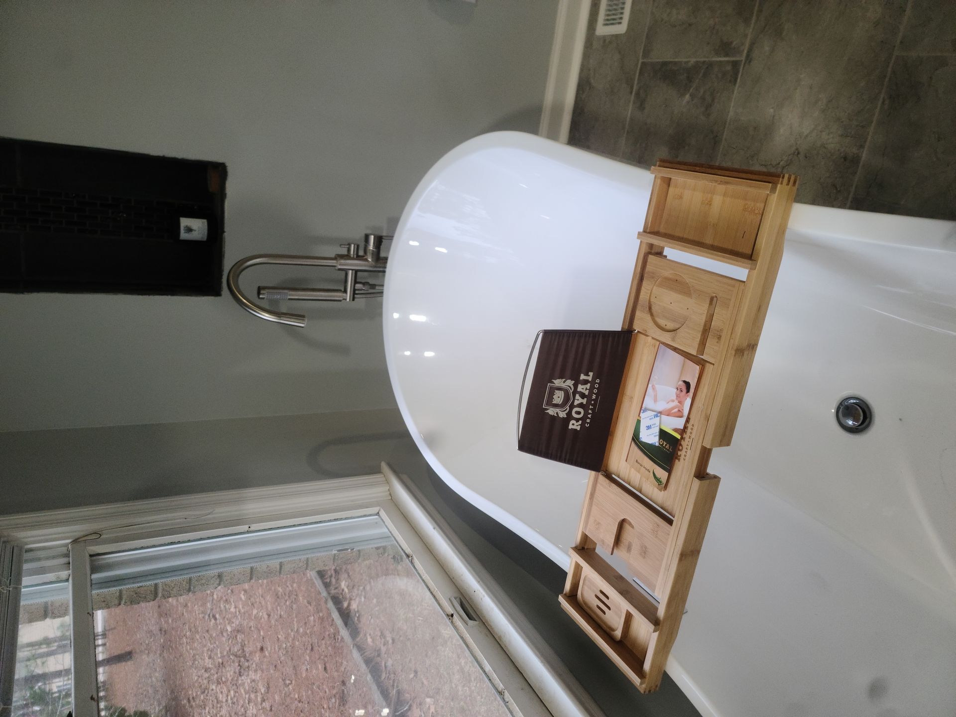 Bathroom with white bathtub, wooden tray, and window, shown sideways.