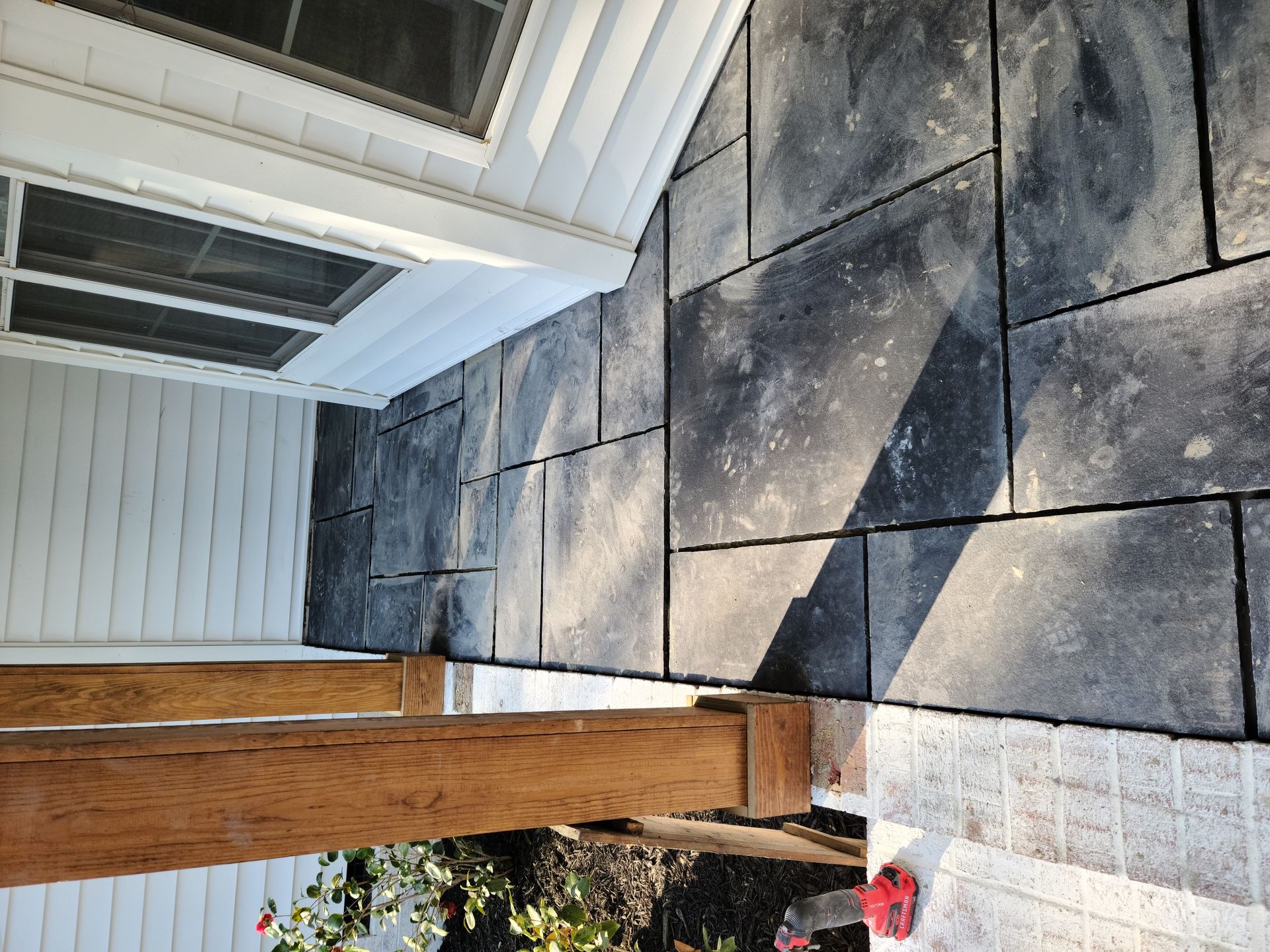 Concrete patio with large gray pavers beside a wooden post and white house siding under an overhang
