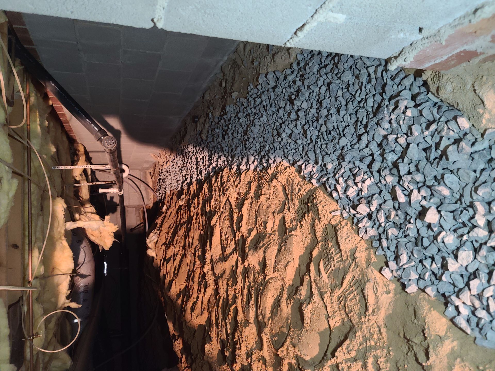Damaged ceiling with exposed beams above a gravel-covered trench or walkway indoors