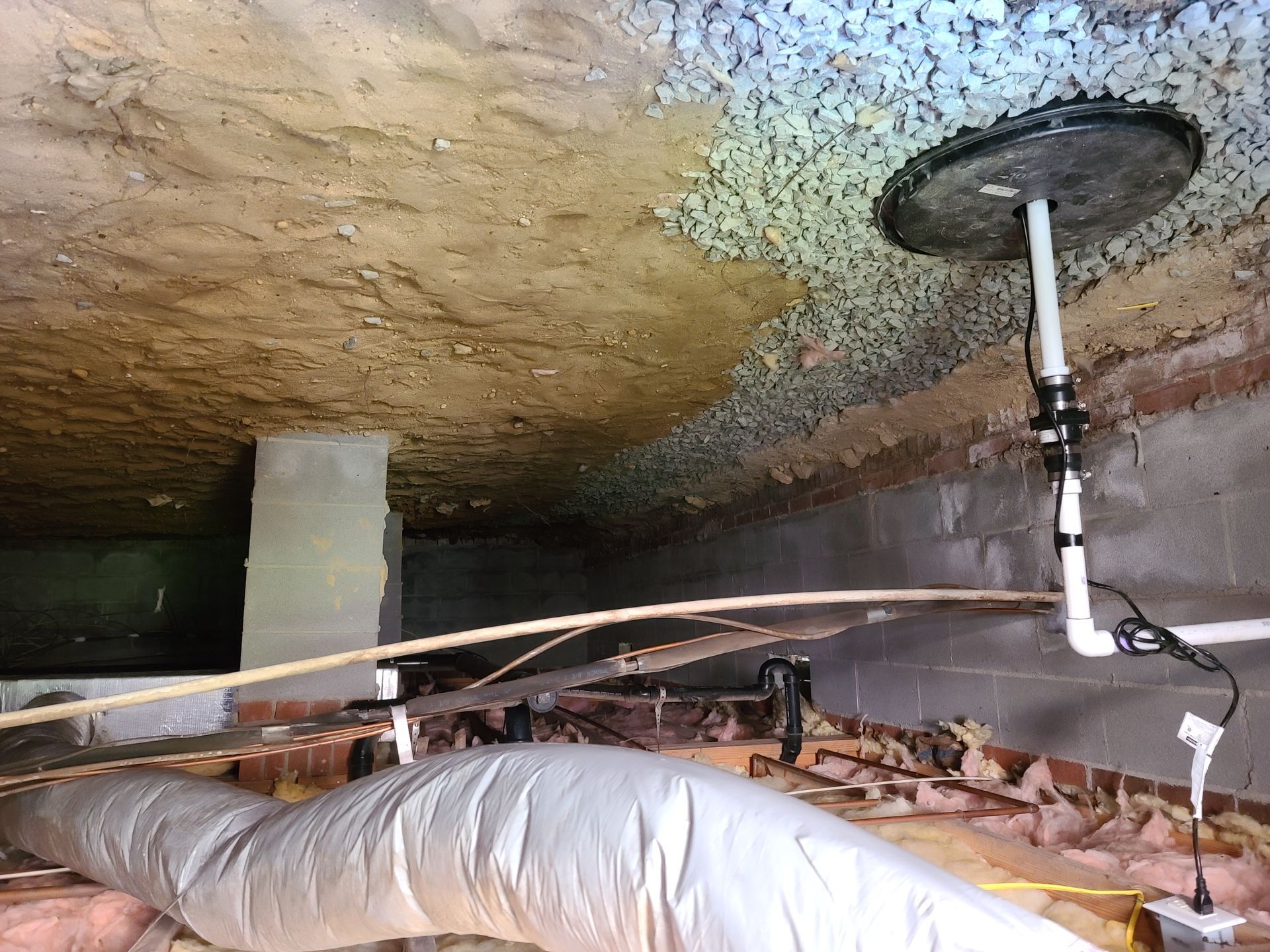 Crawlspace with insulated ductwork, pipes, and a damp, mold-stained ceiling near a vent opening