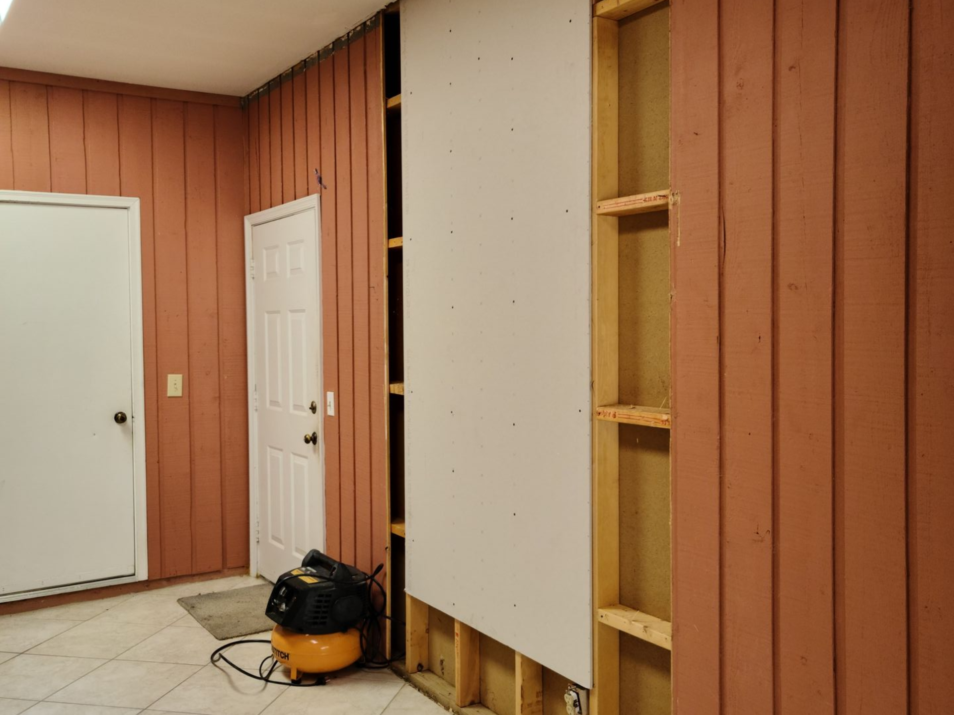 Partially finished room with wood-paneled walls, white doors, and a vacuum cleaner on the floor