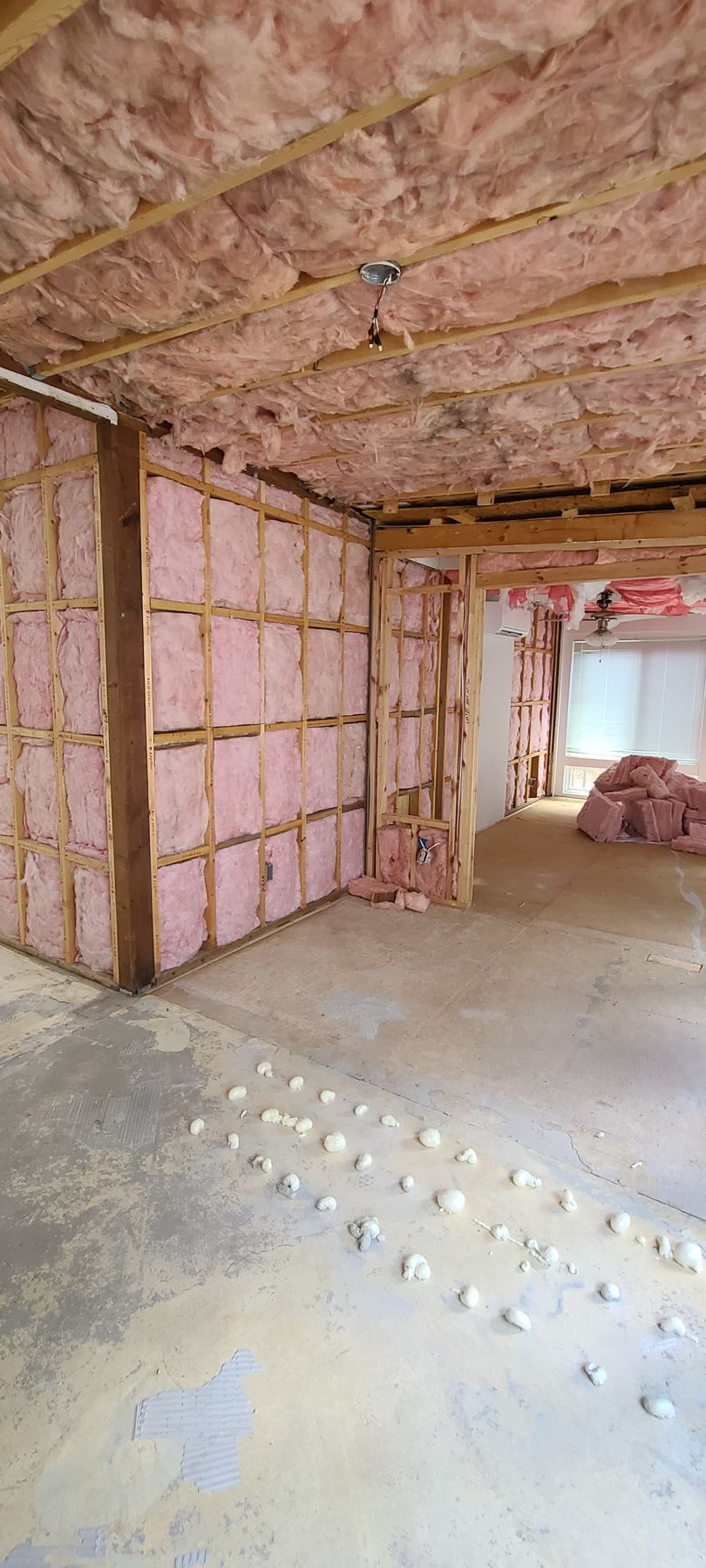 Insulated unfinished room with pink fiberglass batts on walls and ceiling, concrete floor, and doorway to another space