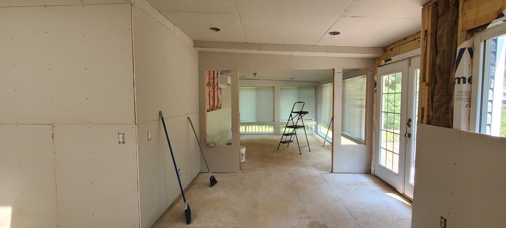 Empty unfinished room with drywall, tools, and a ladder in a bright interior under renovation
