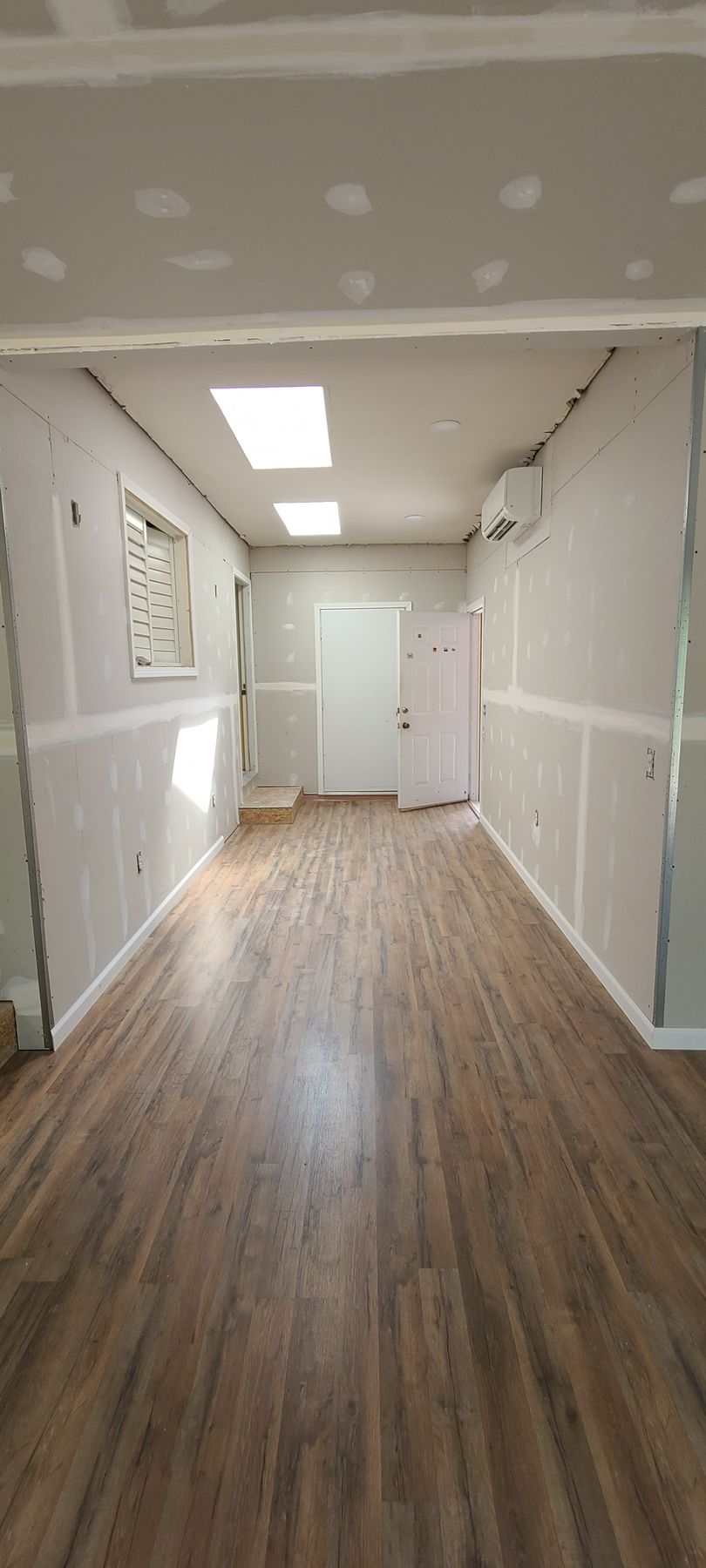Empty hallway with wood-look flooring, white walls, and fluorescent ceiling lights.
