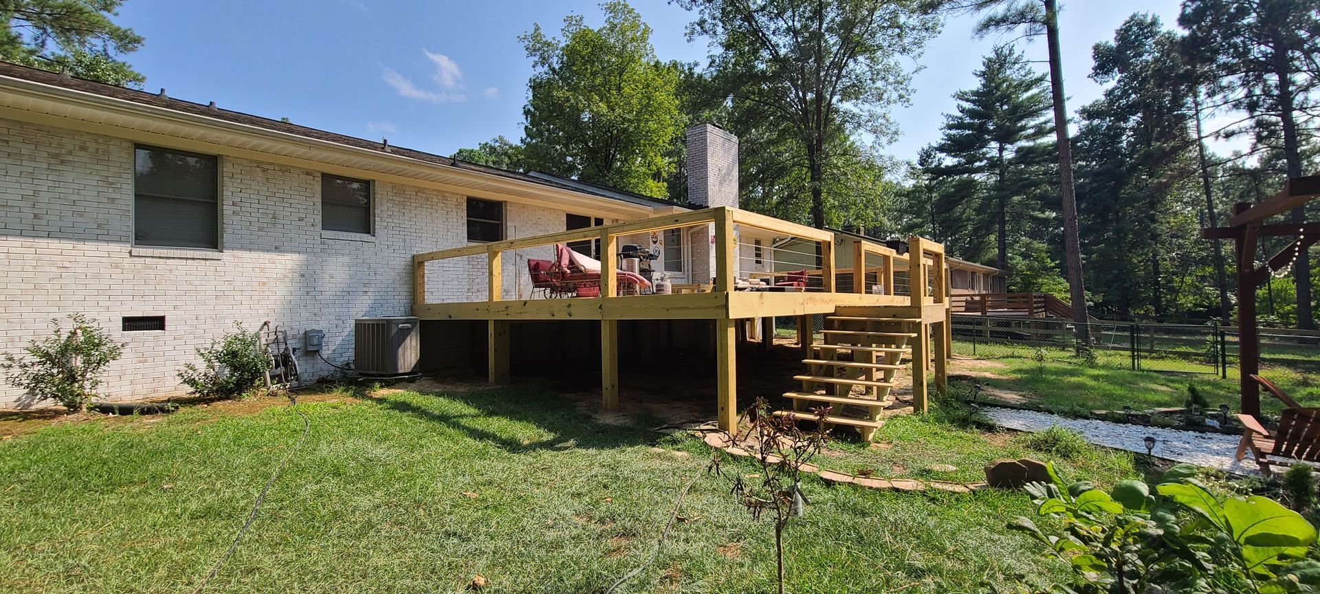 Wooden deck attached to a brick house in a sunny backyard with trees and lawn