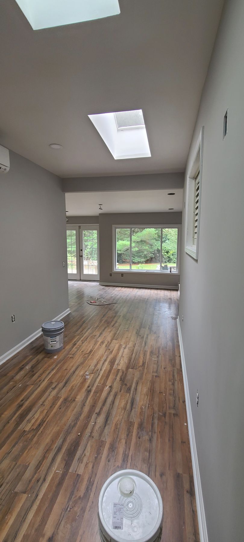 Empty narrow room with hardwood floors, white walls, skylight, and large rear windows overlooking greenery