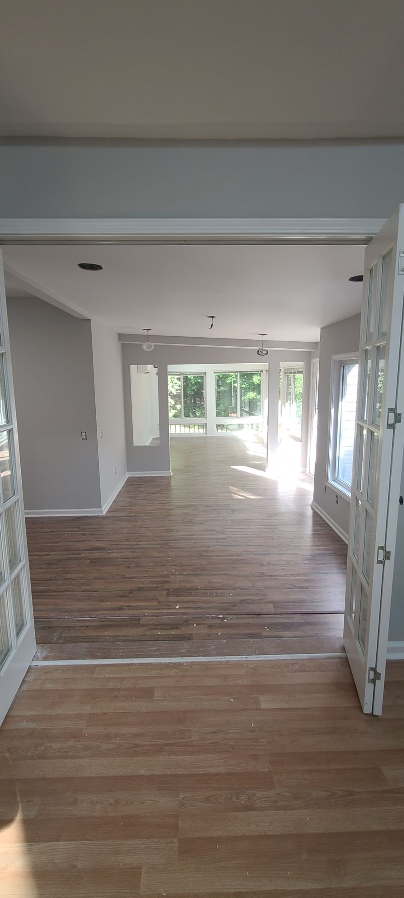 Empty unfurnished room with light wood floors and large windows opening to a bright patio.