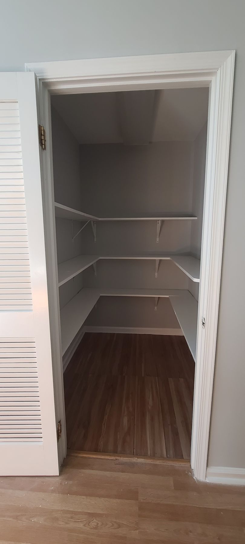 Open closet with white shelves and wood floor in a hallway