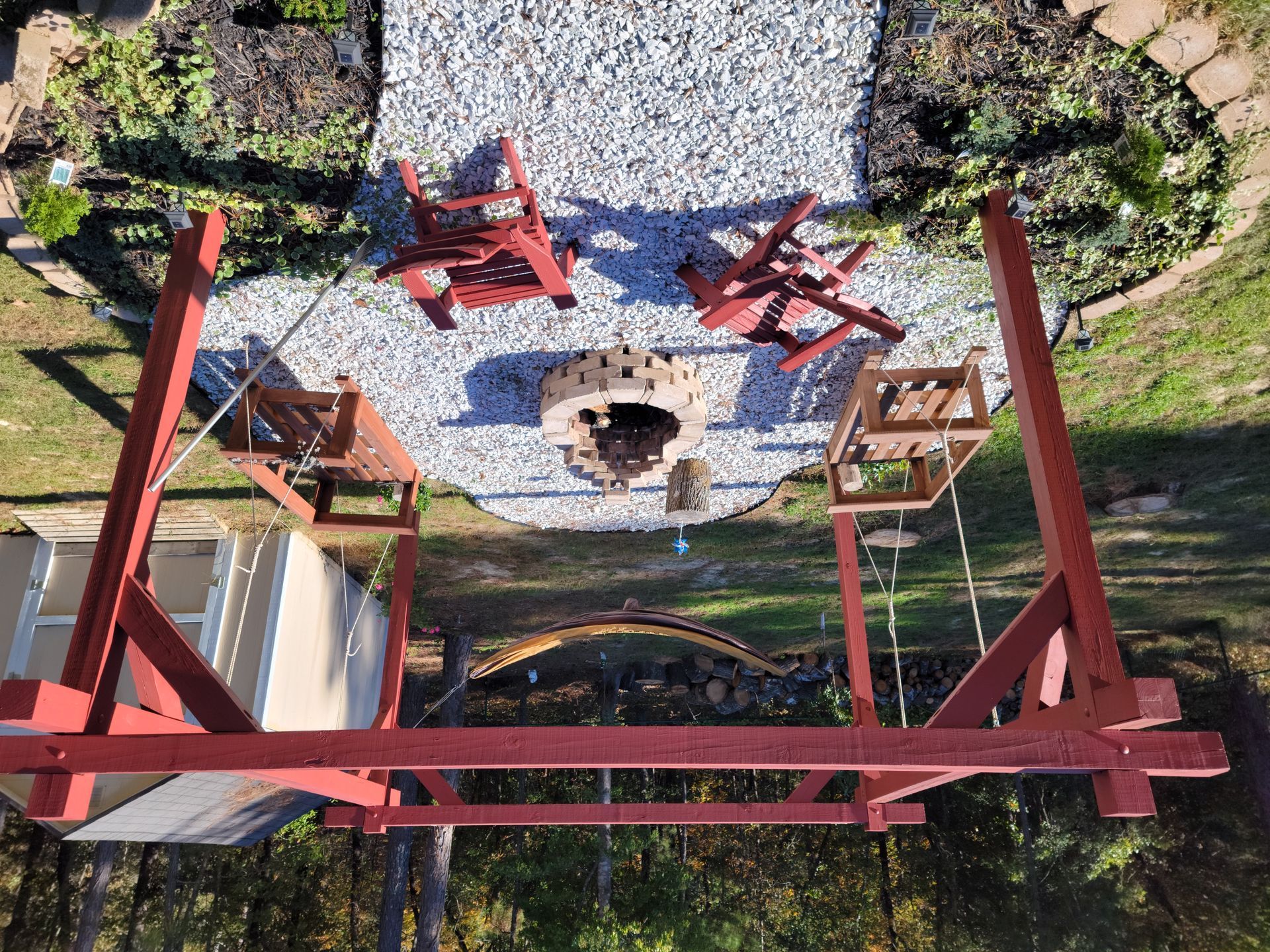 Red metal structure surrounding a circular stone fire pit in a landscaped garden path area