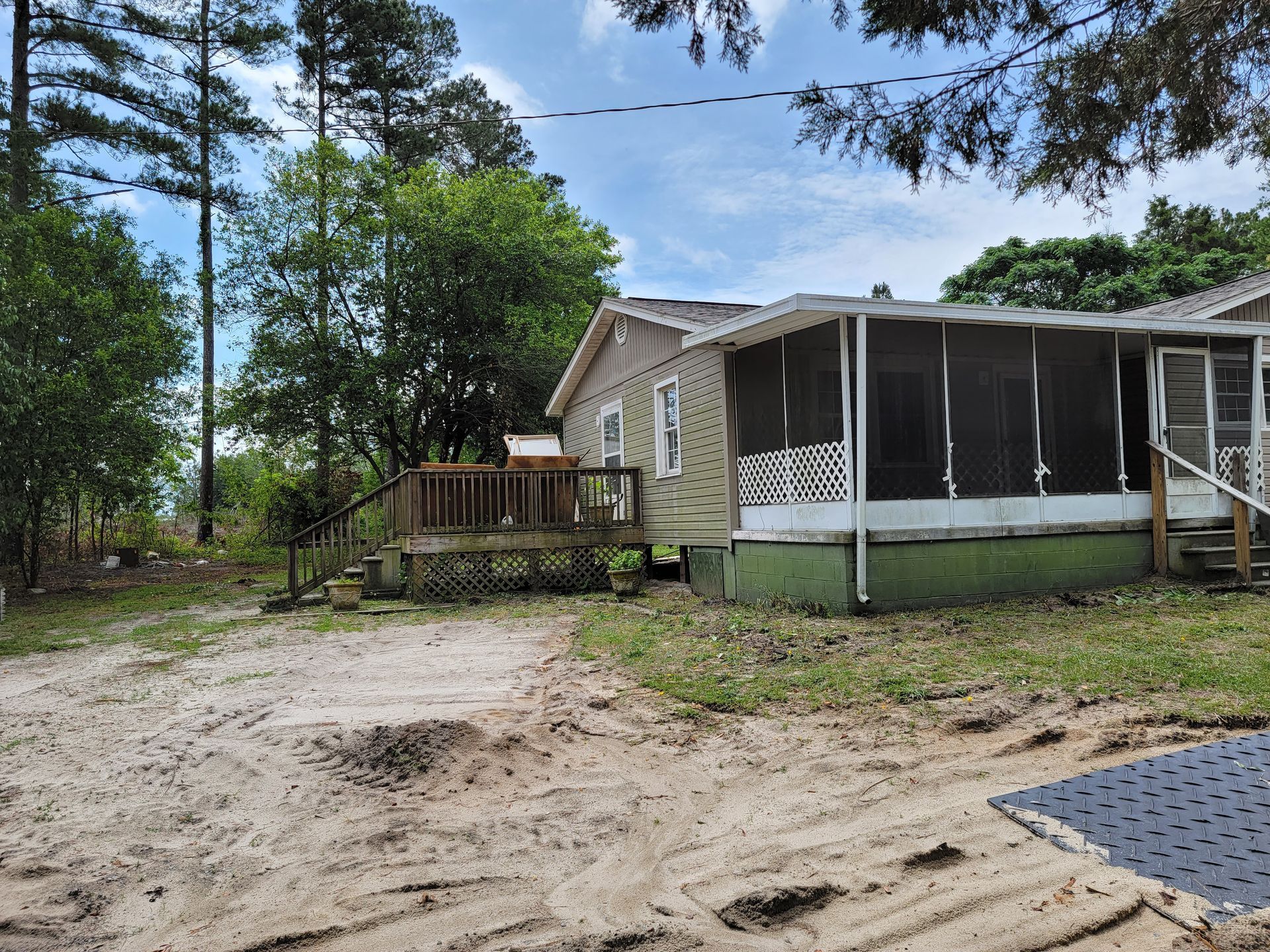 Small beige house with screened porch beside a sandy yard and trees under a cloudy sky