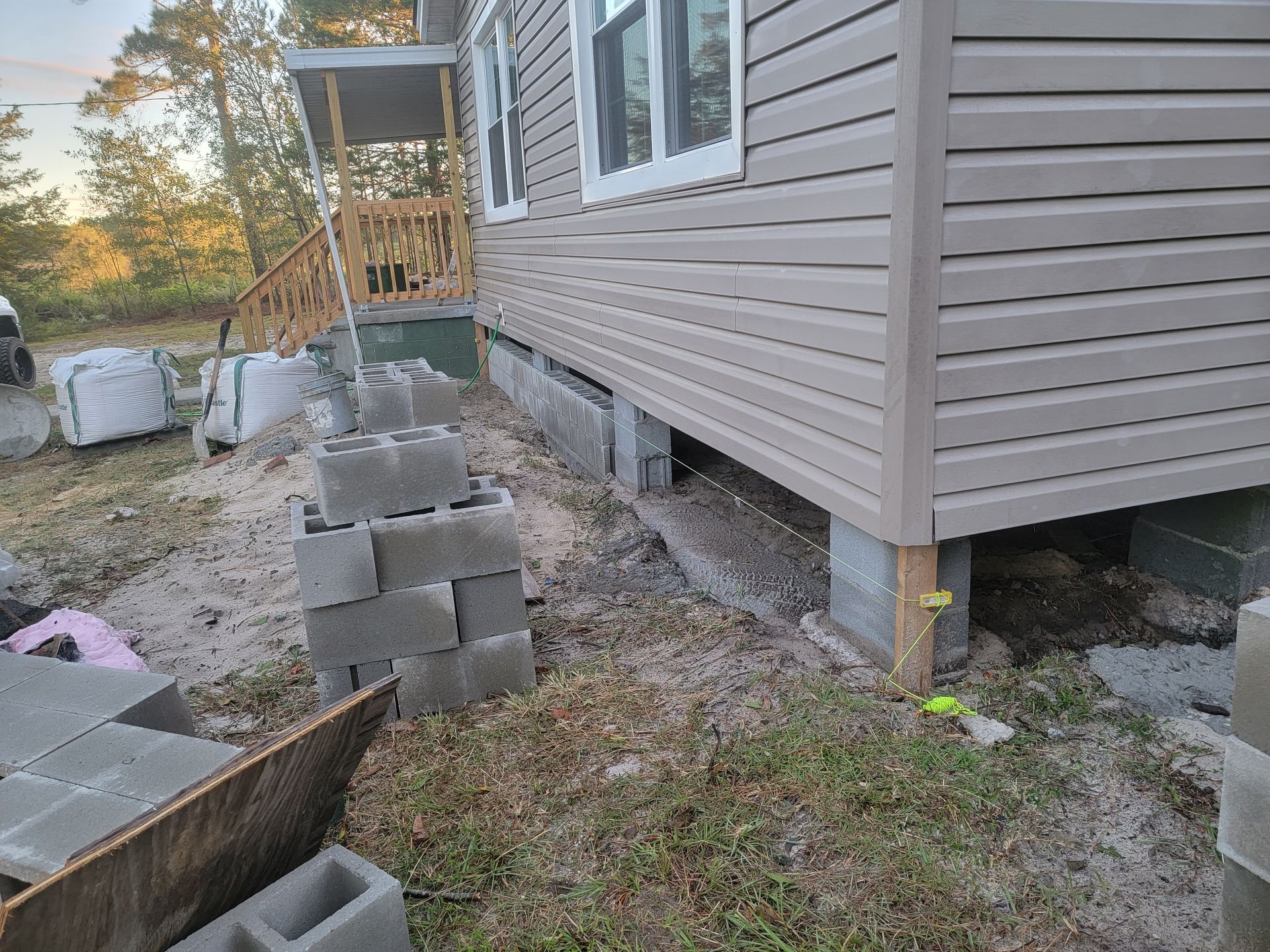 House exterior with stacked cinder blocks and a wheelbarrow beside the foundation underway on a sloped yard