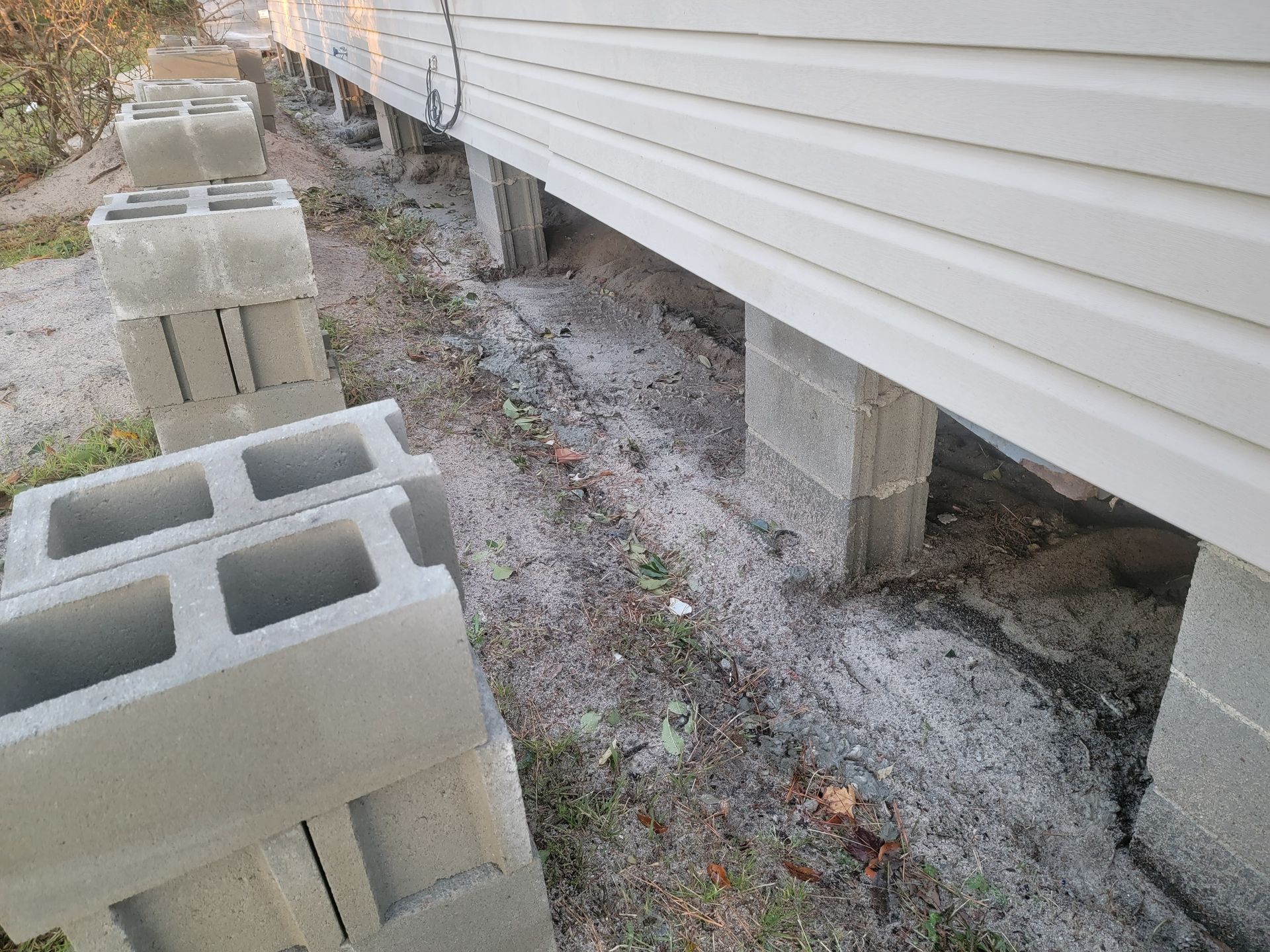 Cinder blocks supporting a house’s side with open crawl space and white vinyl siding