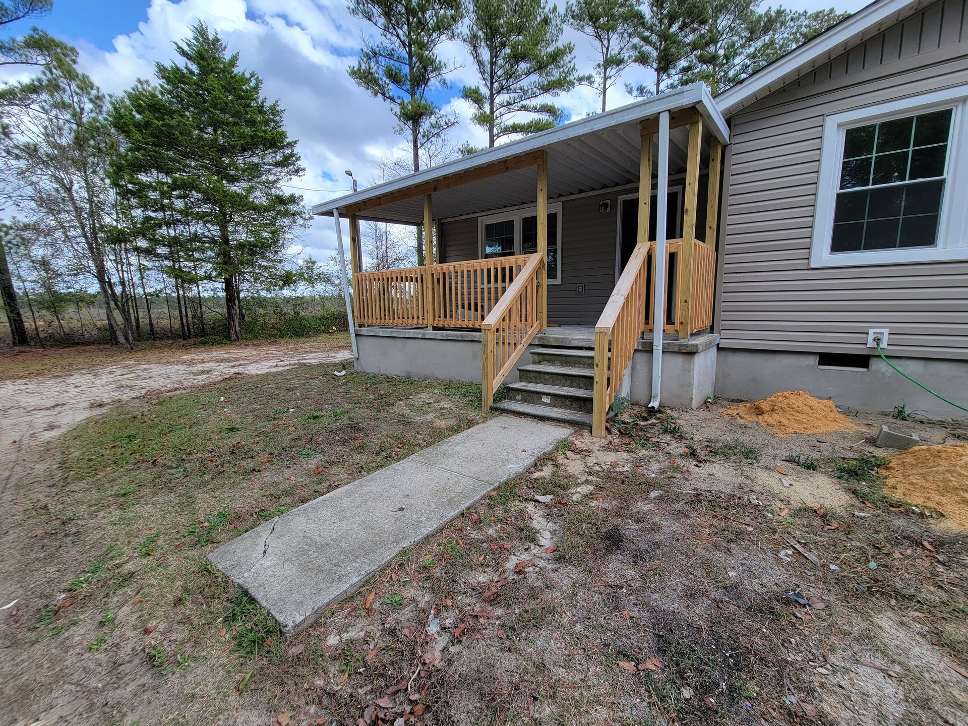 Front porch with steps and wooden ramp leading to a tan house in a wooded yard