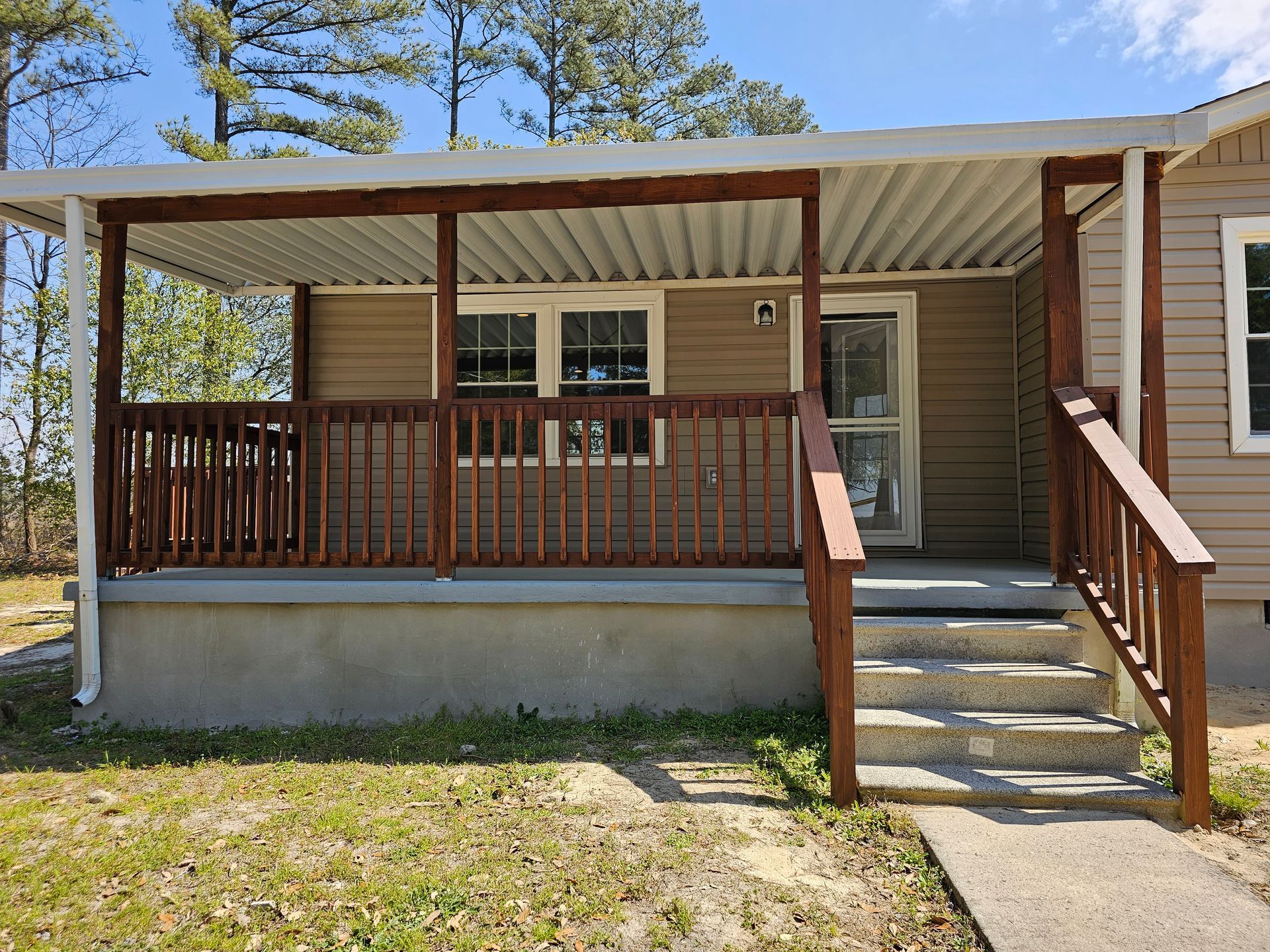 Porch and front steps of a small house with brown railings and beige siding under a covered roof