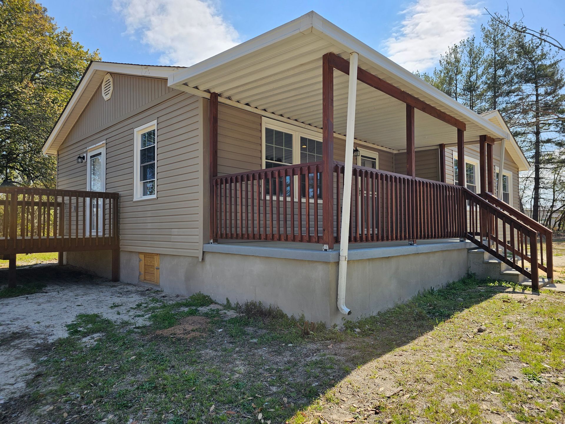Small tan house with a covered porch, wooden railing, and front steps on a grassy yard.