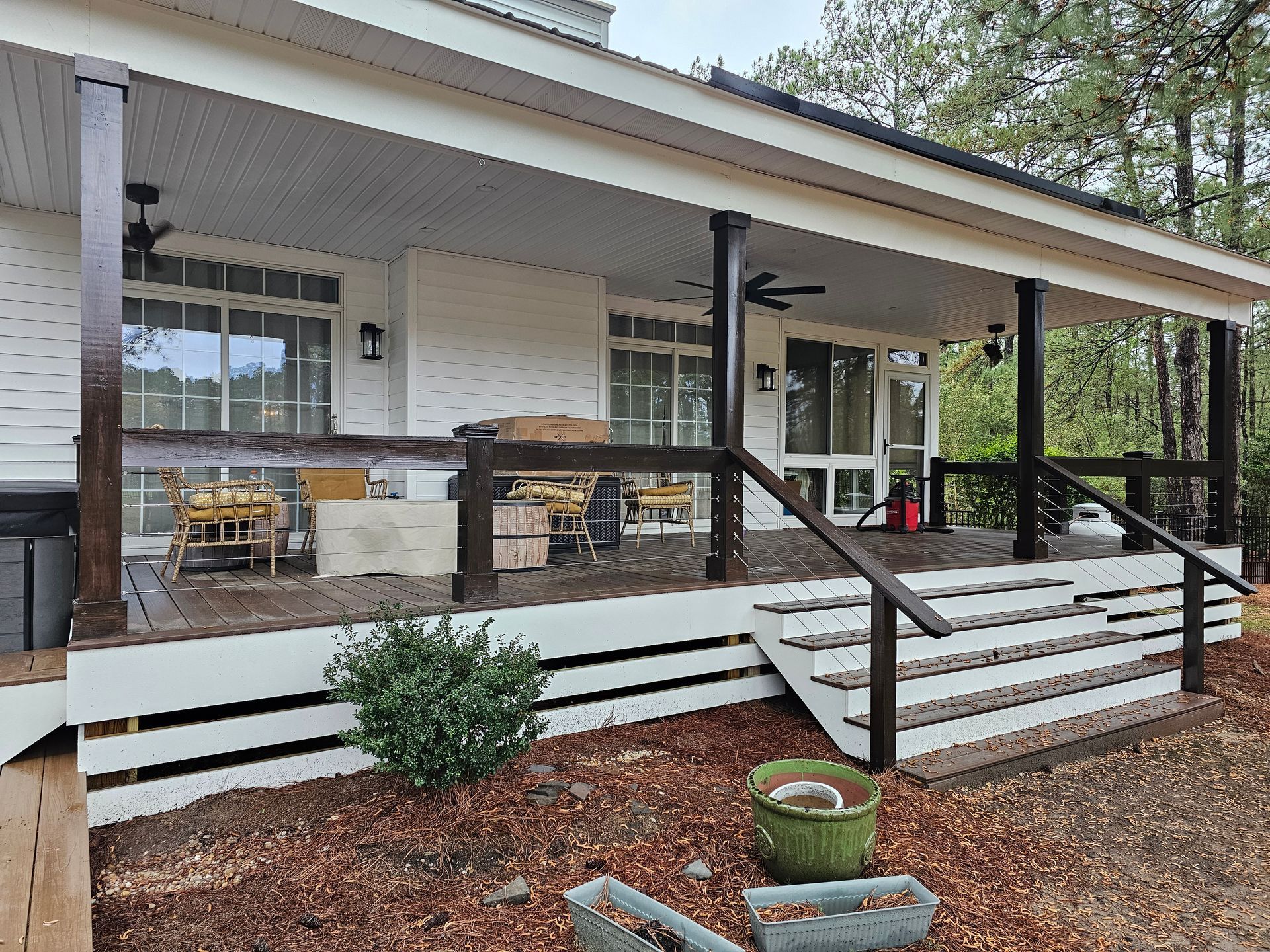 Front porch of a white house with black columns, steps, potted plants, and outdoor seating.