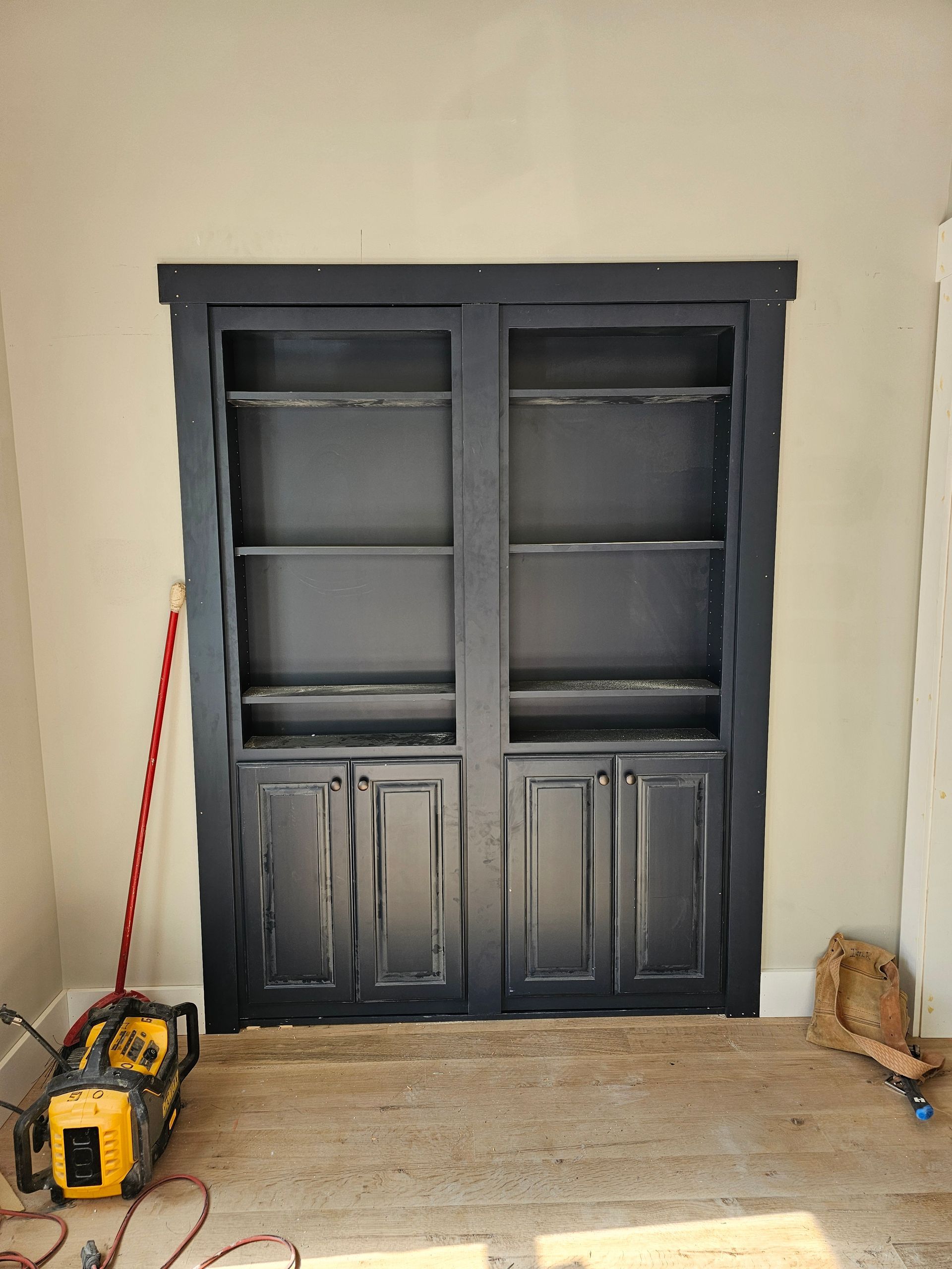 Black double-door cabinet in a room, with a yellow tool on the floor and a broom nearby.