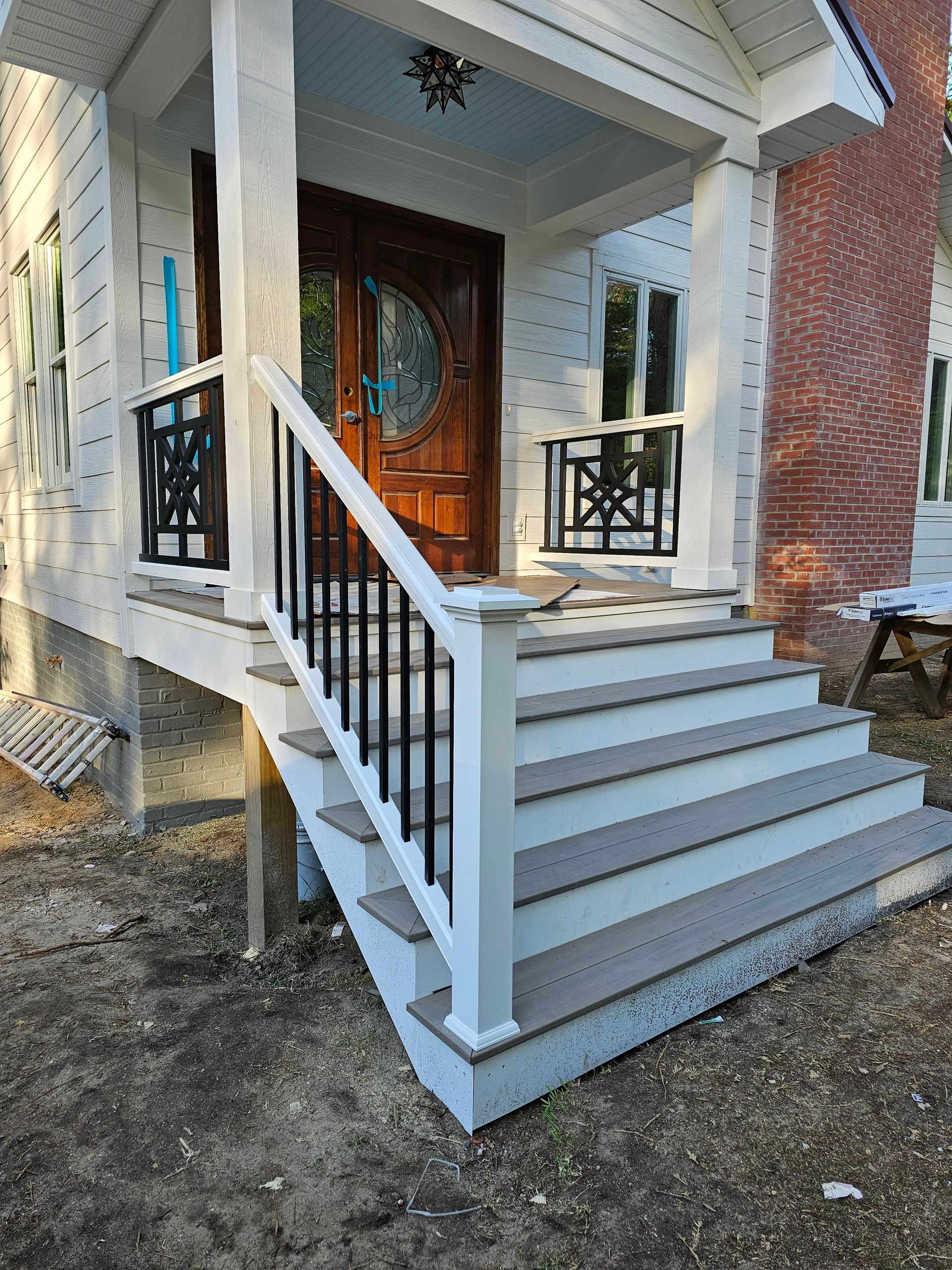 Front porch with white stairs, black railings, and a wooden front door on a brick house