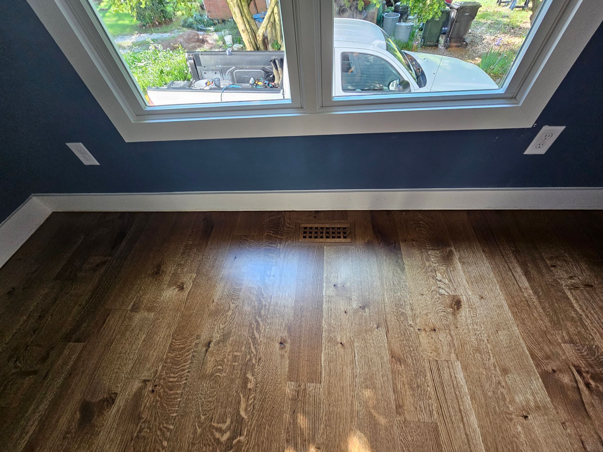 Empty room with dark blue walls, wood floor, and a window looking out to a driveway.