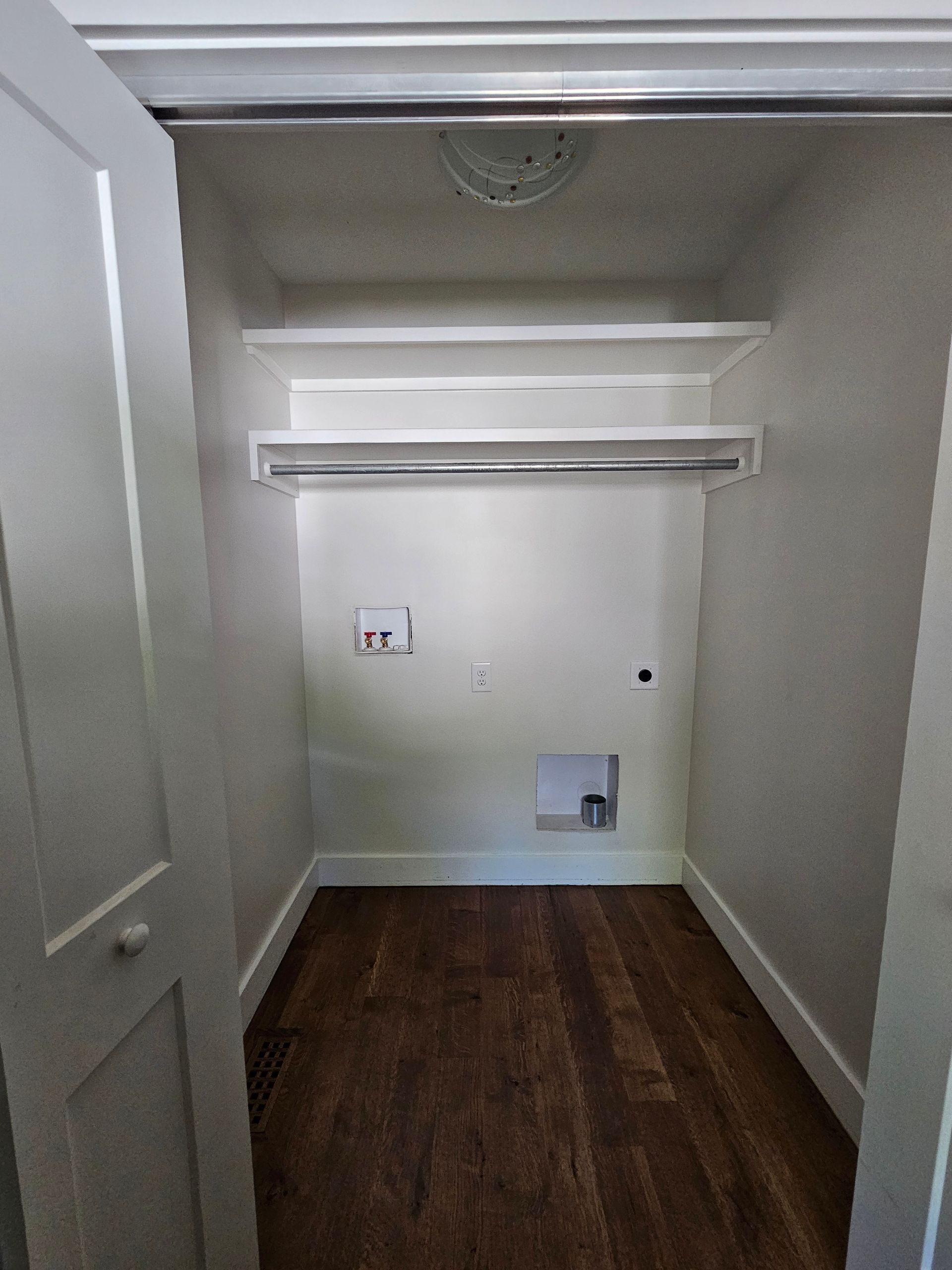 Small empty closet with white walls, wood floor, shelf, hanging rod, and a pet door opening at the back.