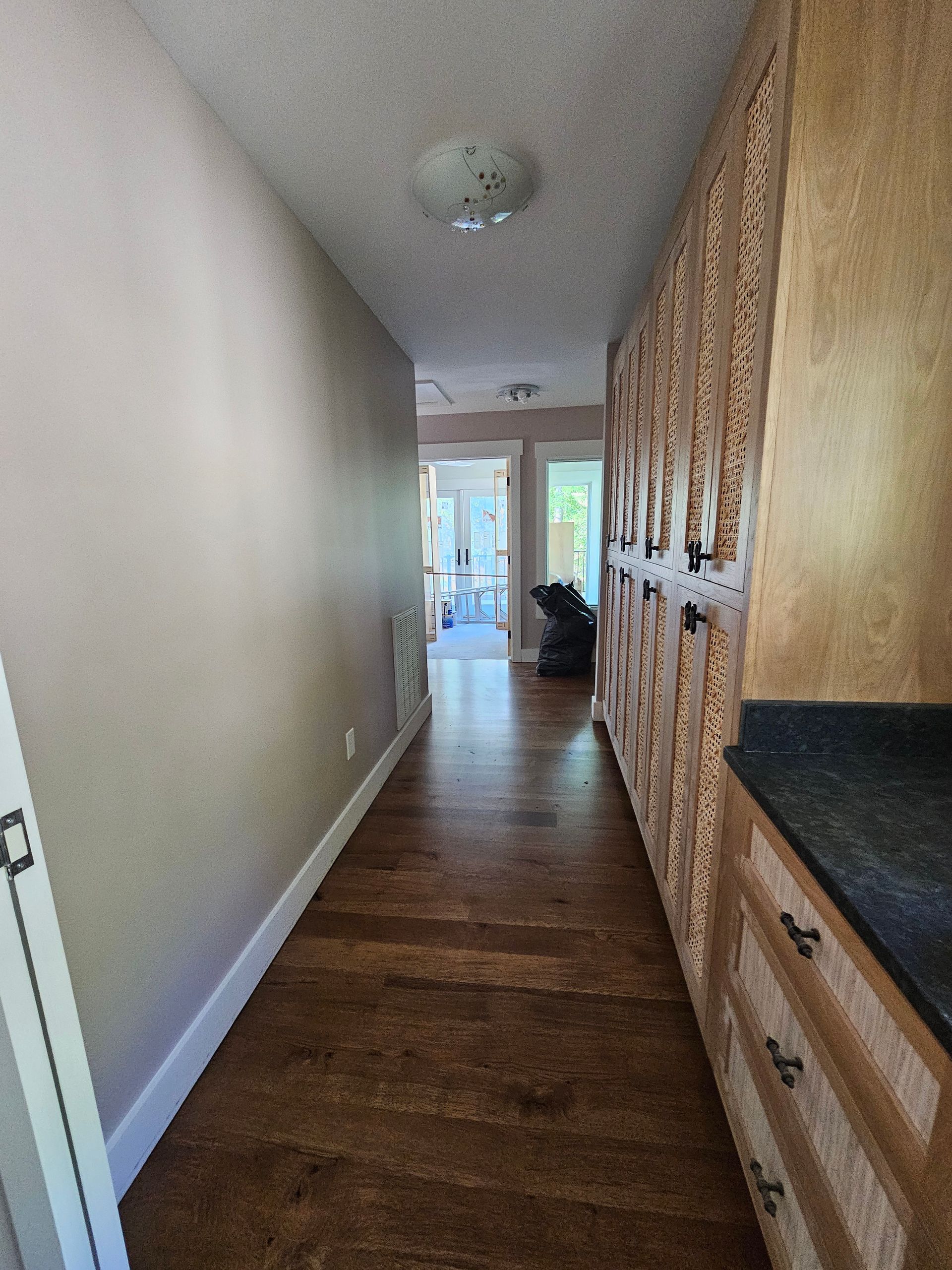 Narrow hallway with wood flooring, built-in cabinets, and a bright doorway at the far end.