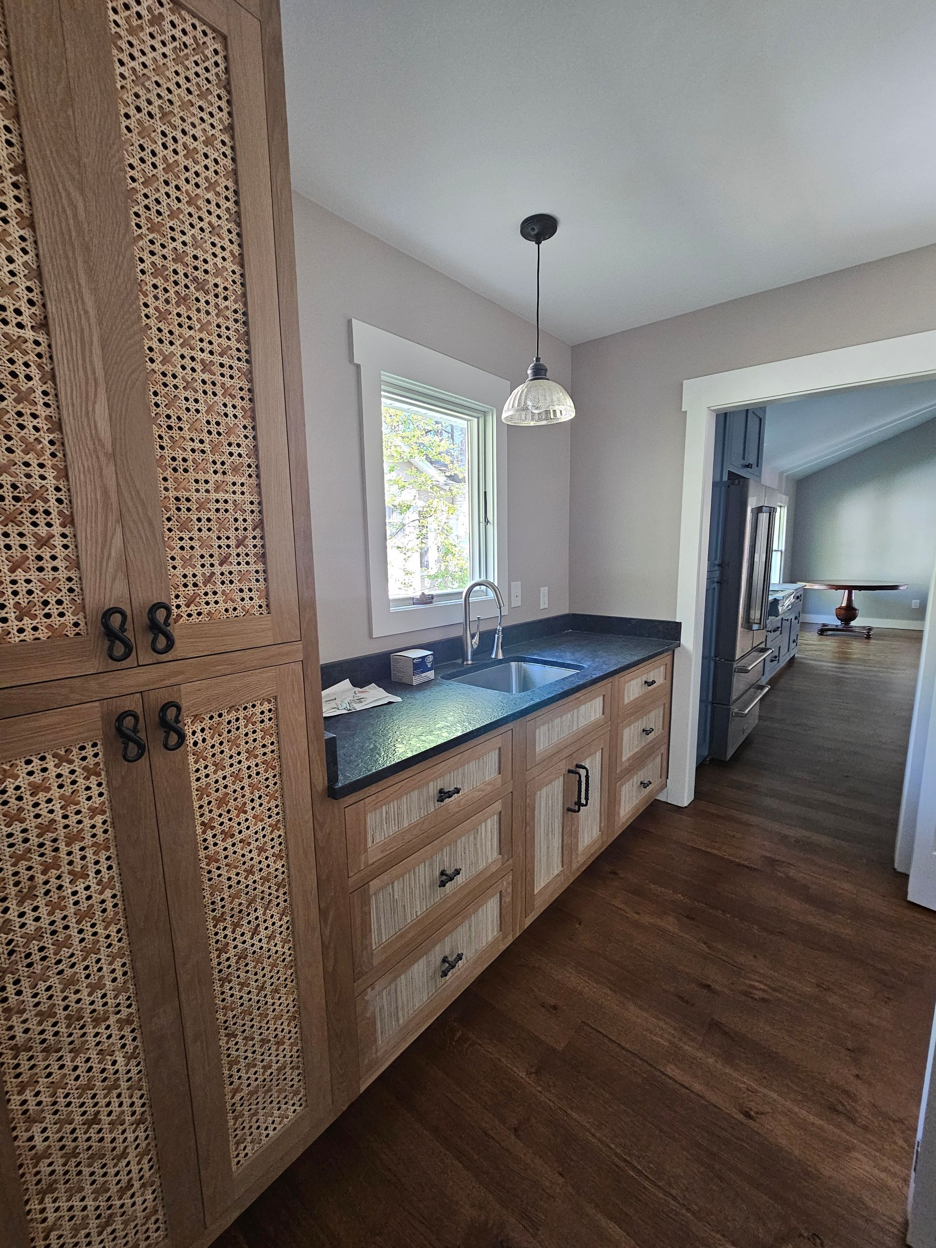 Narrow kitchen with wood cabinets, black countertop, and doorway to a living room.