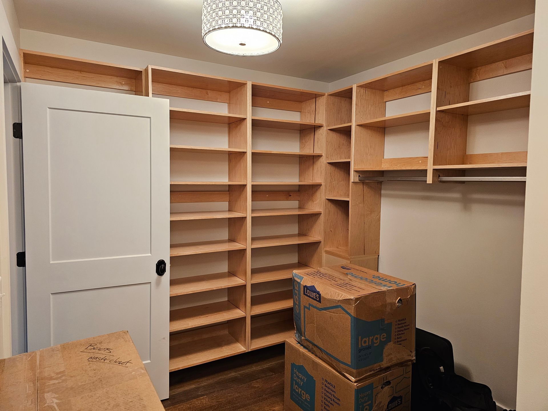 Built-in wooden shelves in a closet or office room with boxes on the floor and a white door.