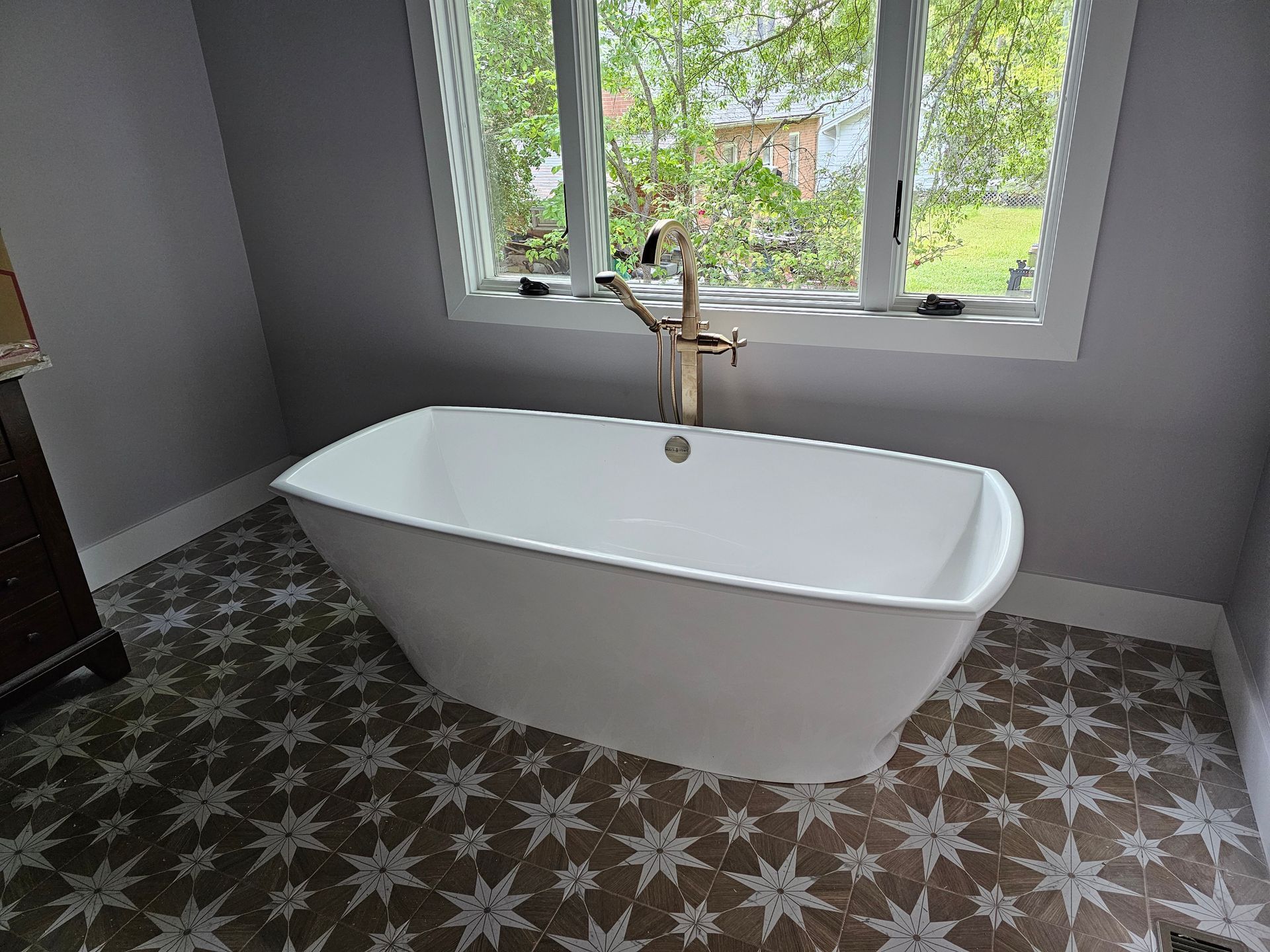 Modern bathroom with a freestanding white bathtub, brass faucet, and patterned tile floor by a window
