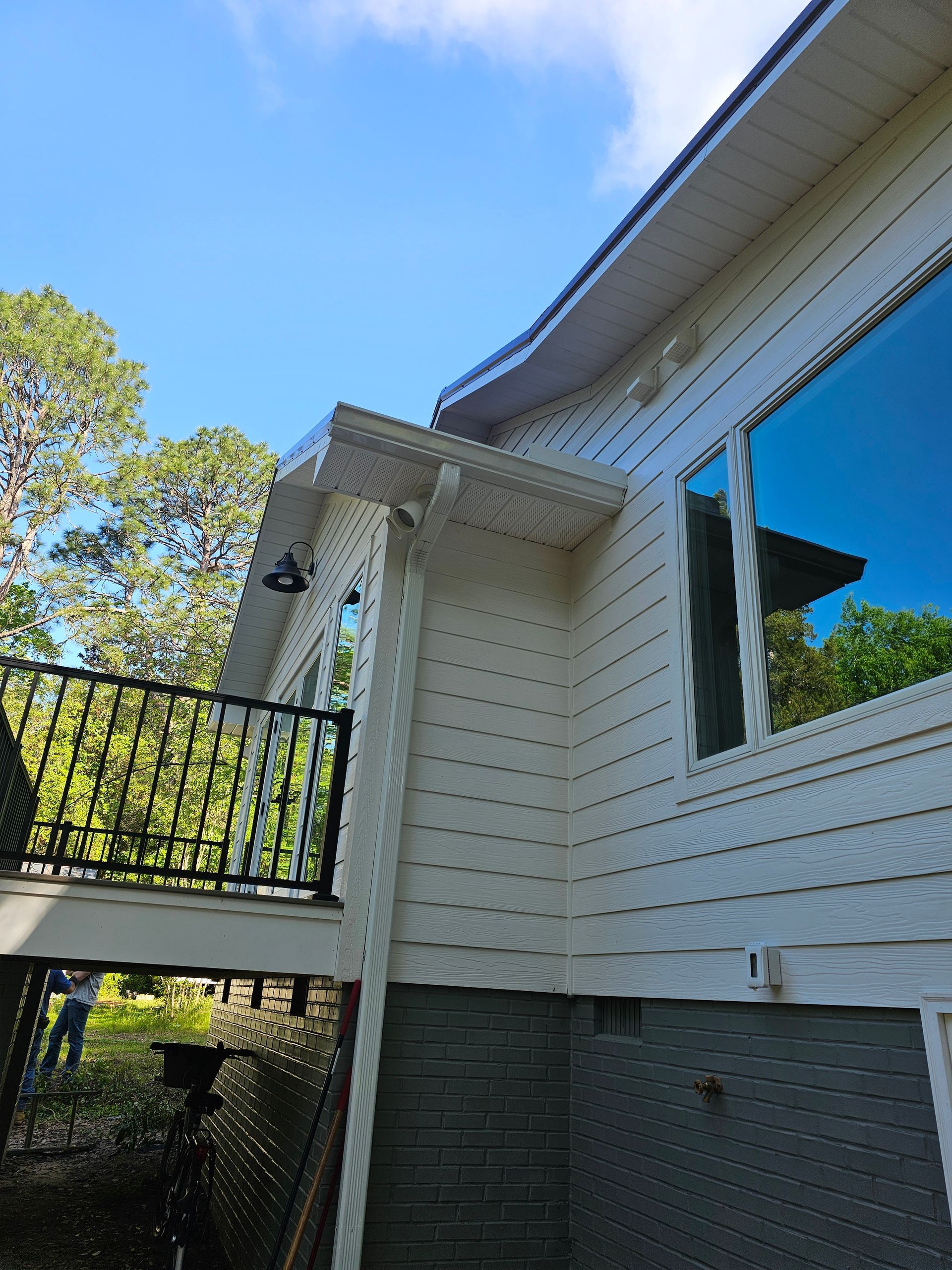 White house exterior with blue-trimmed windows, balcony railing, and tree against a clear blue sky