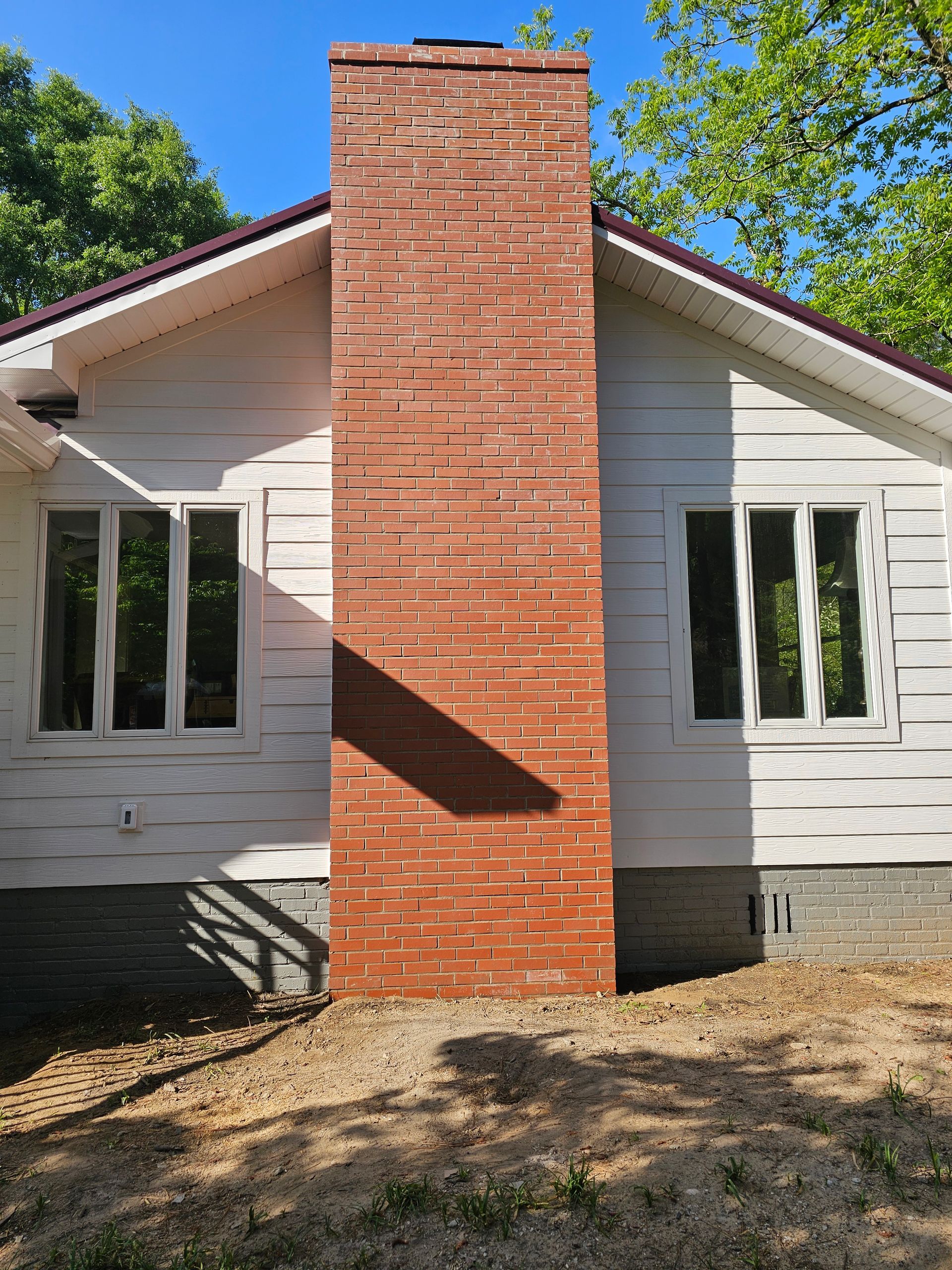 Front view of a white house with a tall red brick chimney centered between two windows.