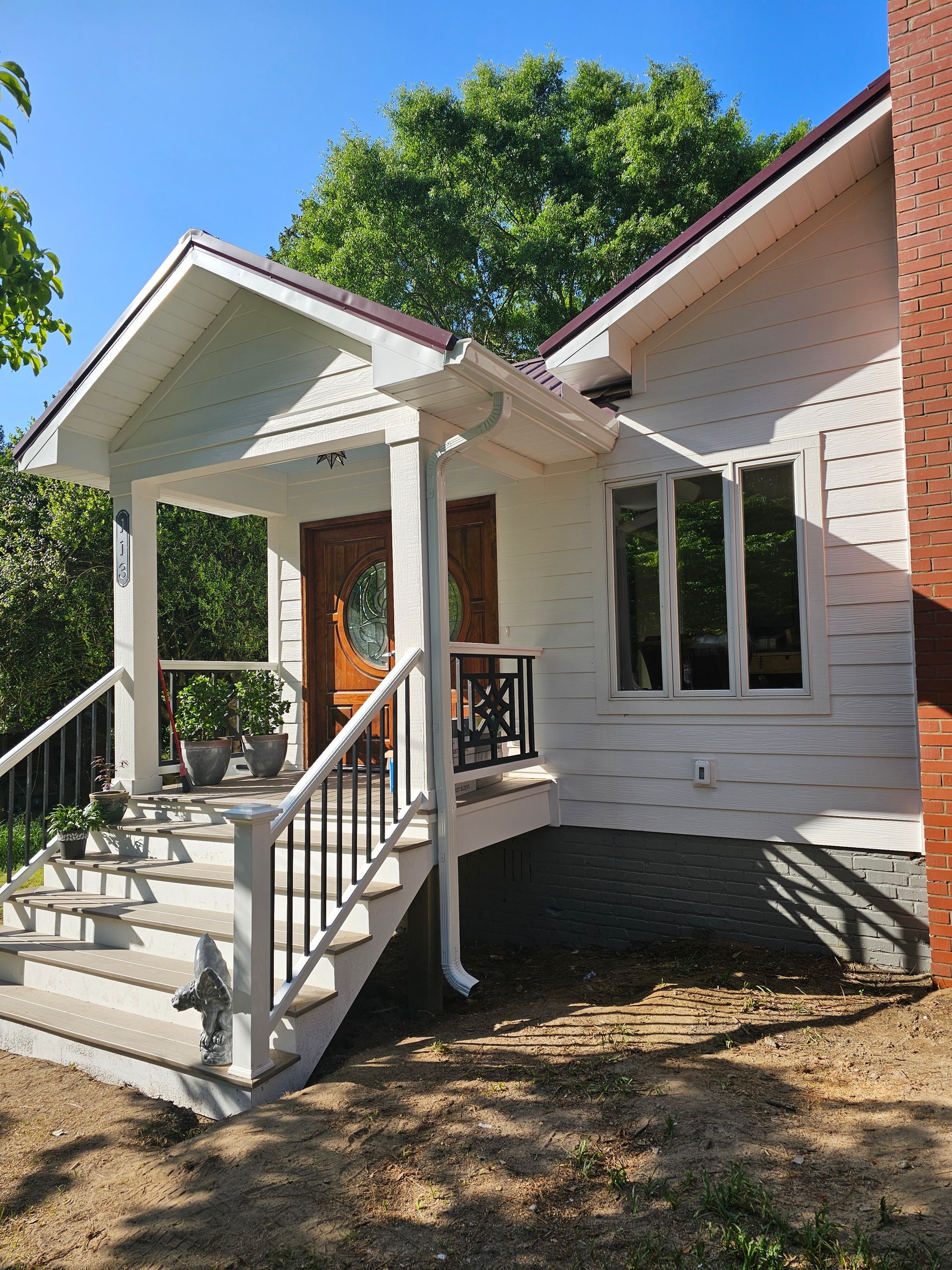 Front porch of a white house with steps, railings, and a small covered entryway surrounded by trees.