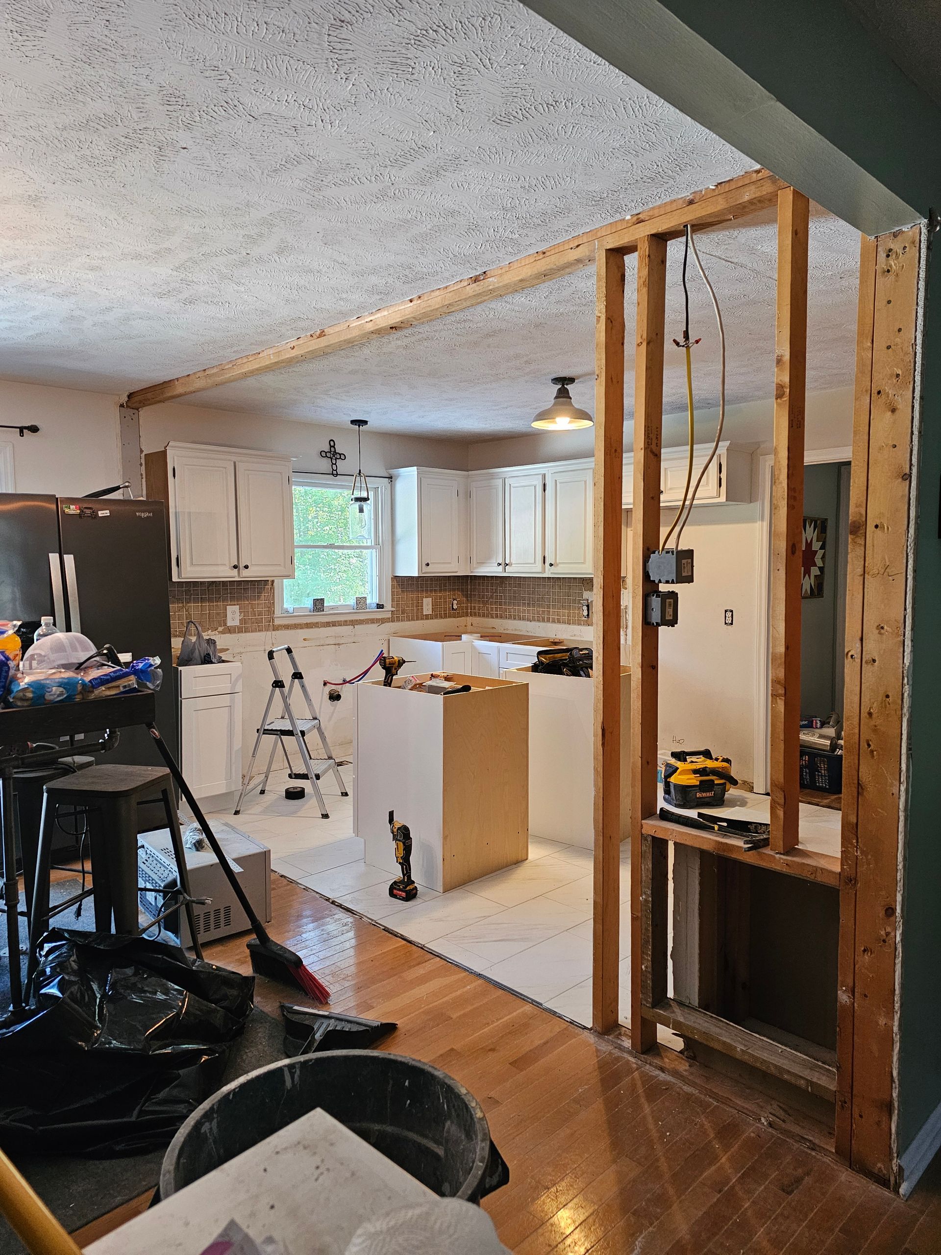 Partially renovated kitchen with exposed studs, white cabinets, ladder, and tools on the floor