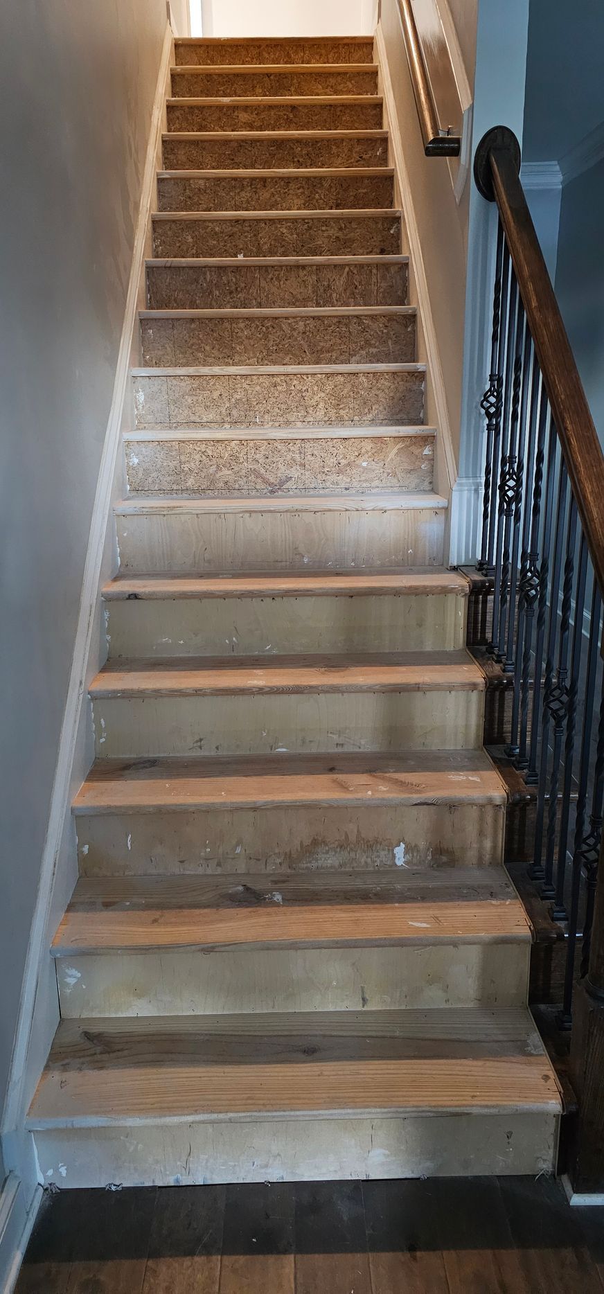 Narrow carpeted staircase with dark wooden railing, leading upward indoors