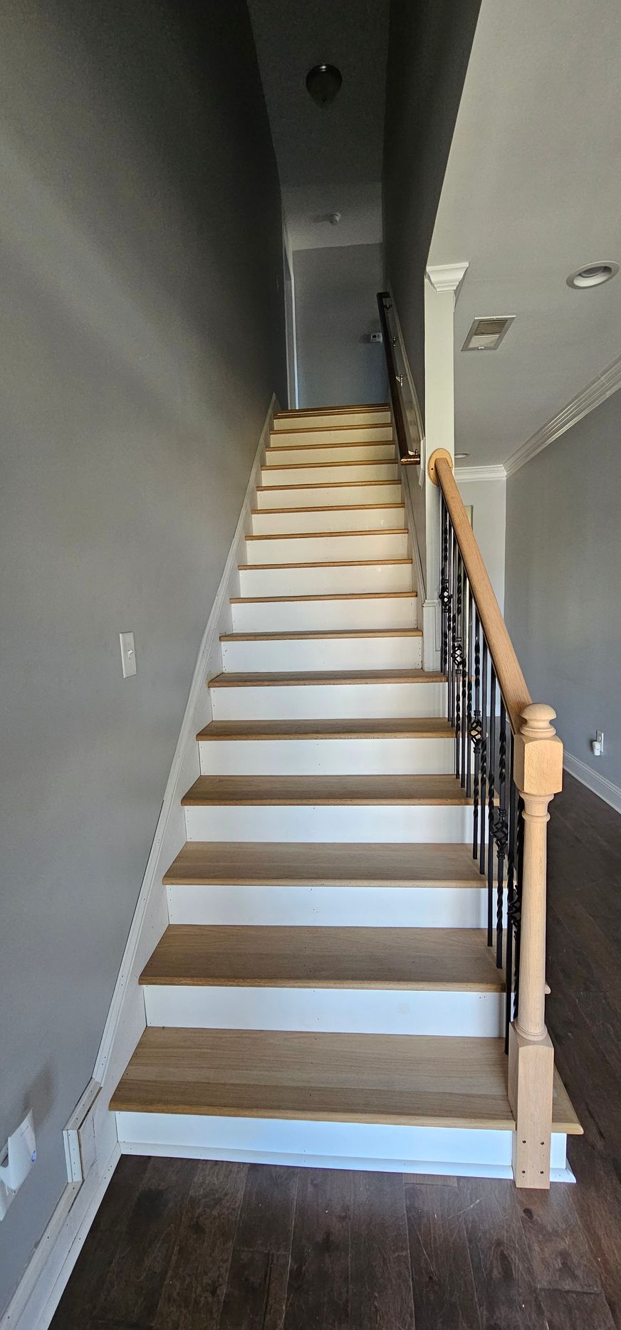 Narrow indoor staircase with beige steps, dark walls, and wooden handrail leading upward