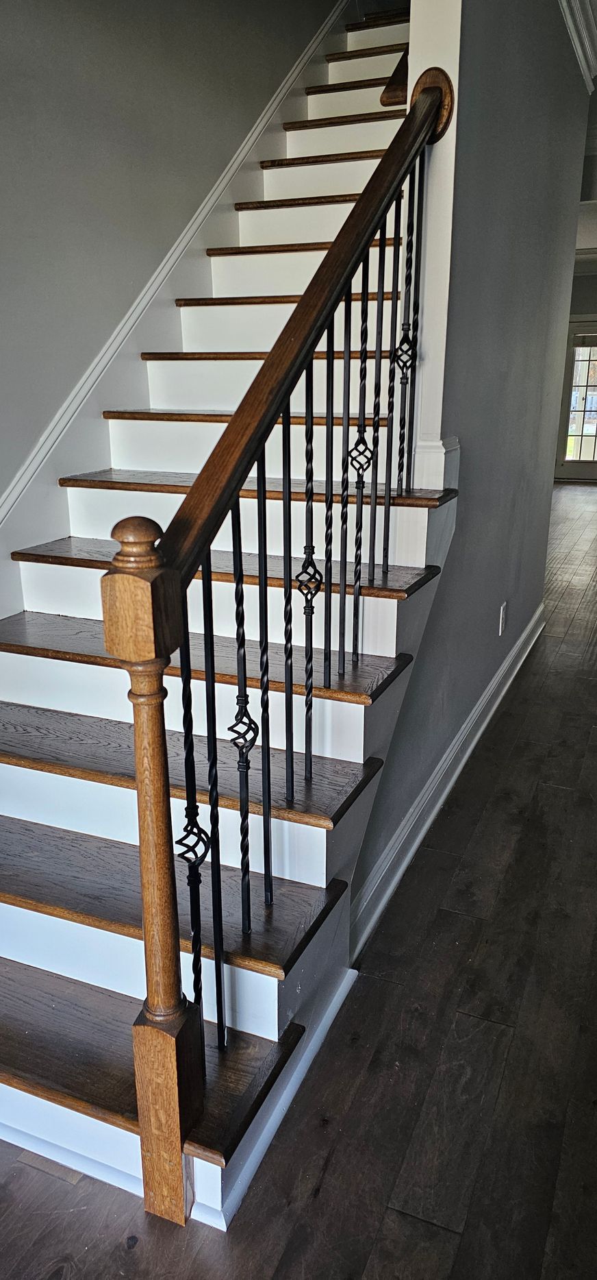 Wooden staircase with white steps, dark metal spindles, and a brown handrail in a hallway.
