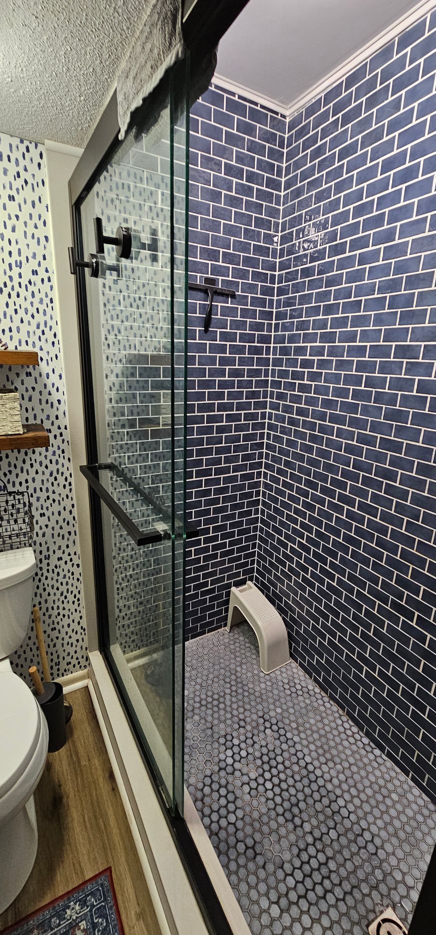 Narrow walk-in shower with blue mosaic tile, glass door, and pebble floor in a small bathroom