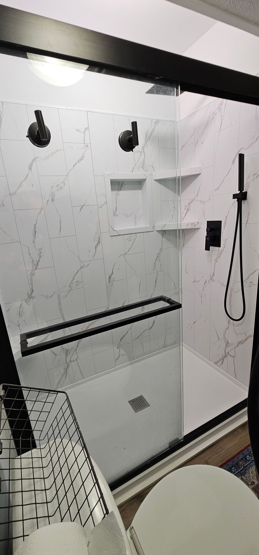 Modern bathroom shower with glass enclosure, marble-look tile, black fixtures, and built-in shelves